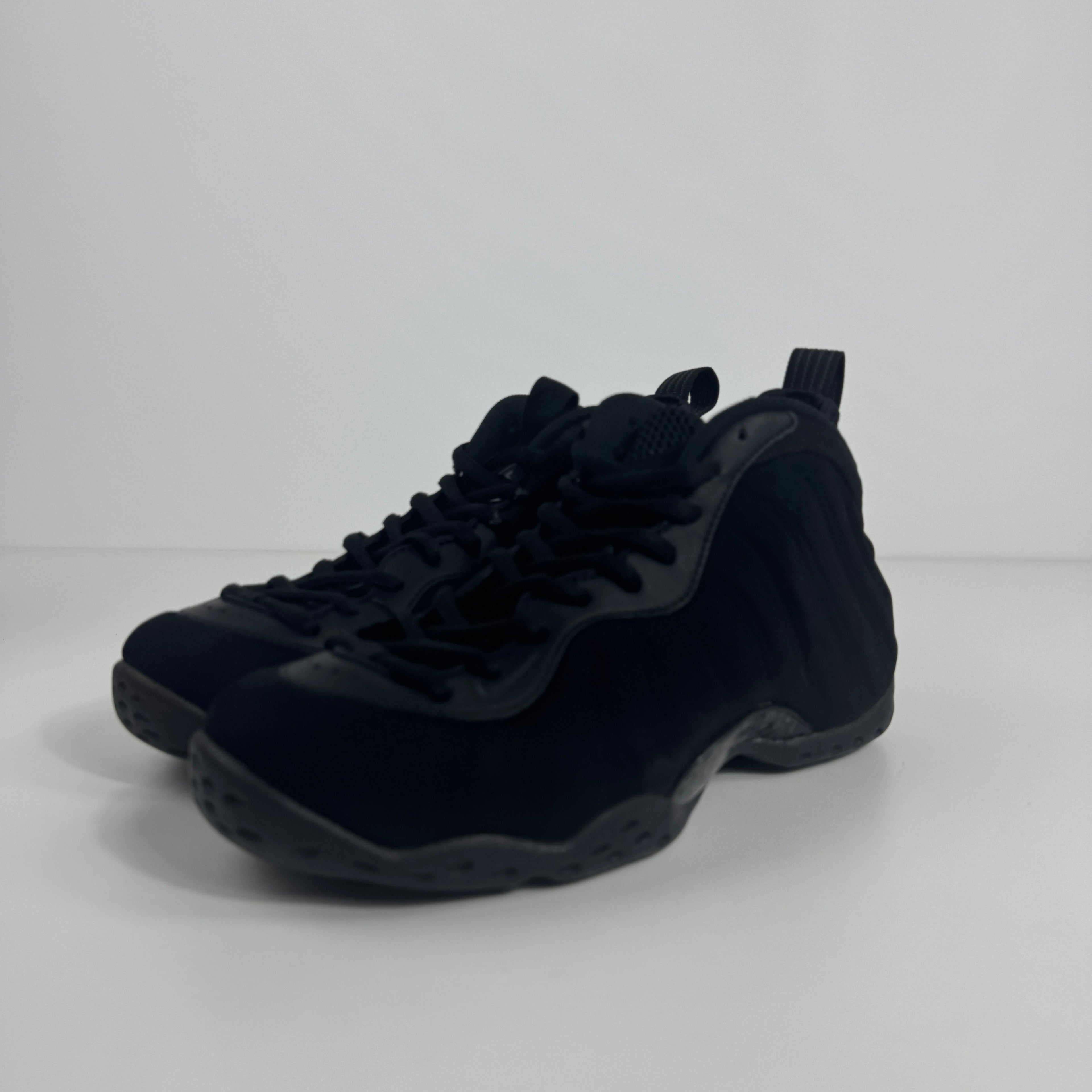 A pair of black Nike basketball trainers with lace-up fronts and textured soles is shown on a white surface with a white background.