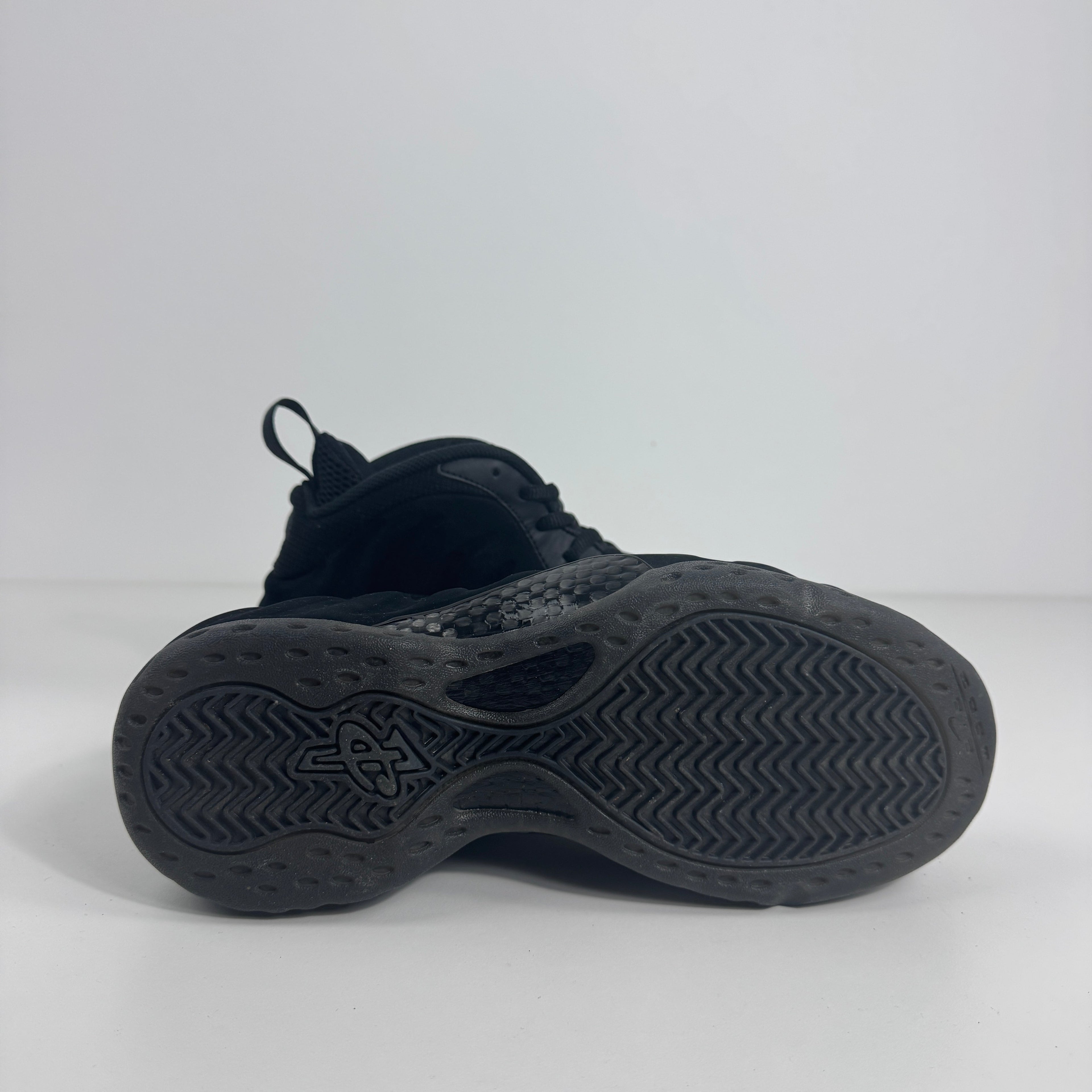 A Nike Air Foamposite One trainer displayed sole up, showing detailed tread pattern and visible cushioning on a white background.