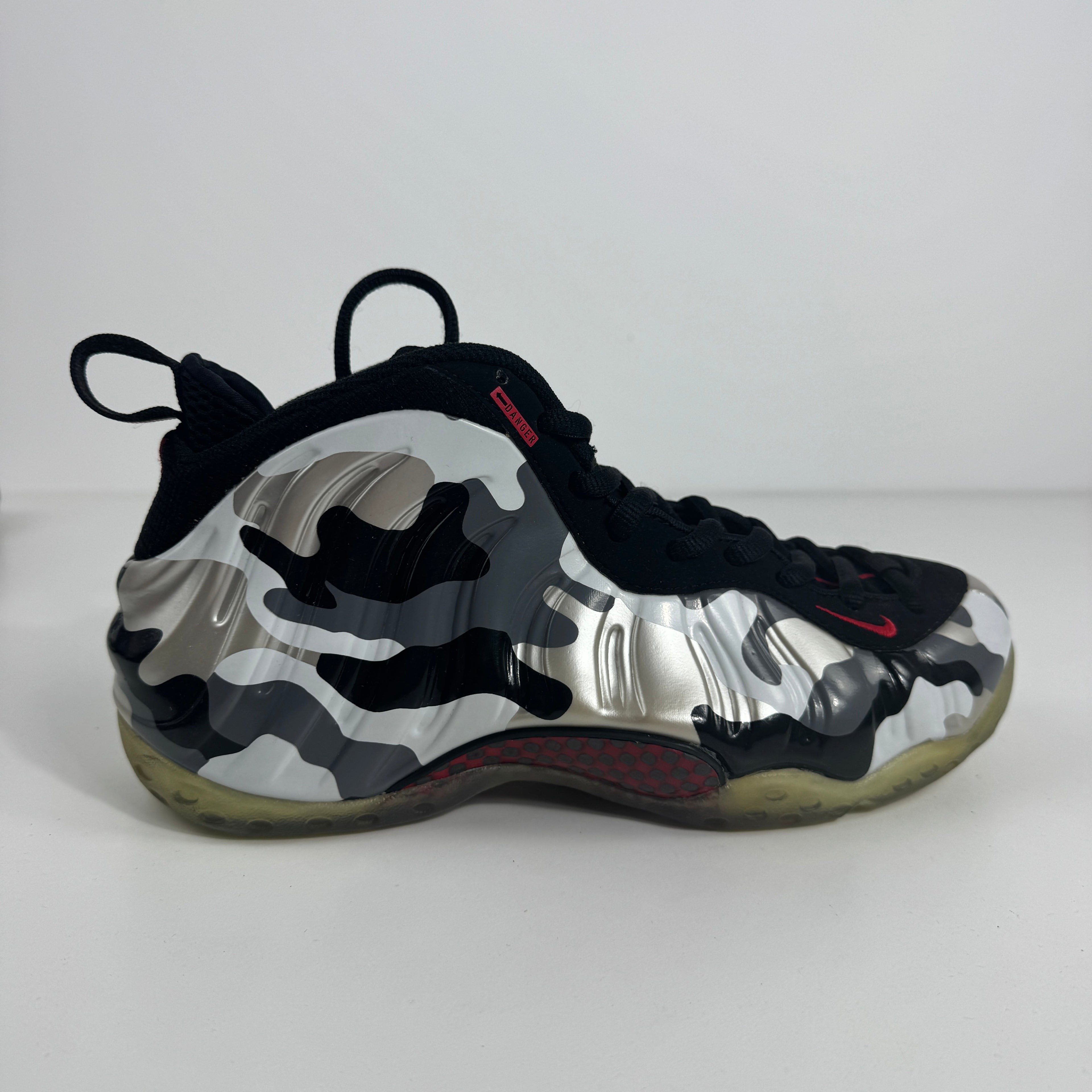 Nike trainer with a black, white and grey camo upper, black laces and trim, red details, and a translucent yellow-toned sole on white background.