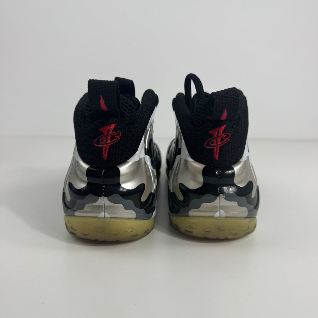 NIKE Air Foamposite One trainers viewed from the back, with a shiny silver and black design, red logo pull tabs and yellowed soles.