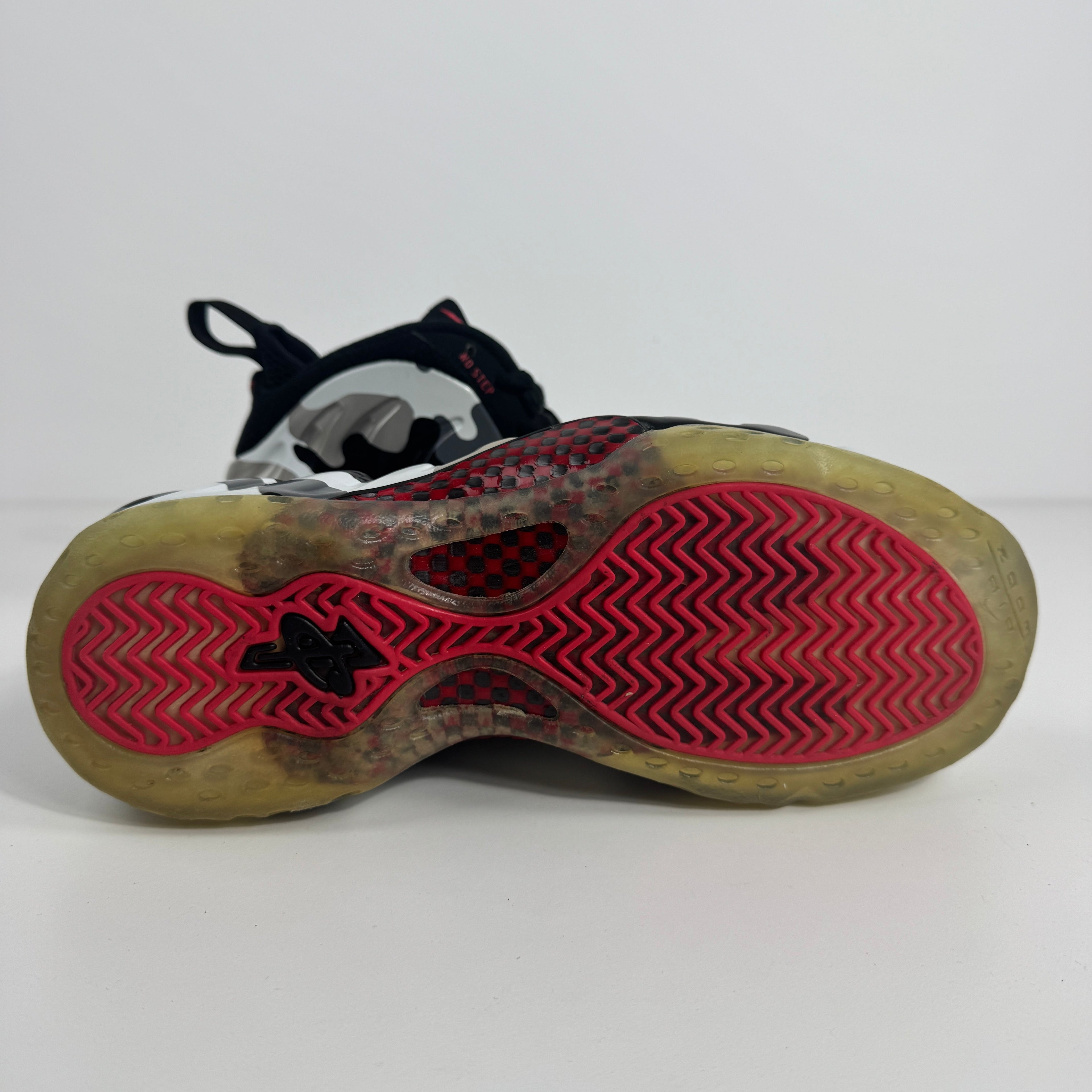 Close-up of a Nike trainer sole with a see-through rubber base, red zigzag tread and black detailing, on a plain white background.