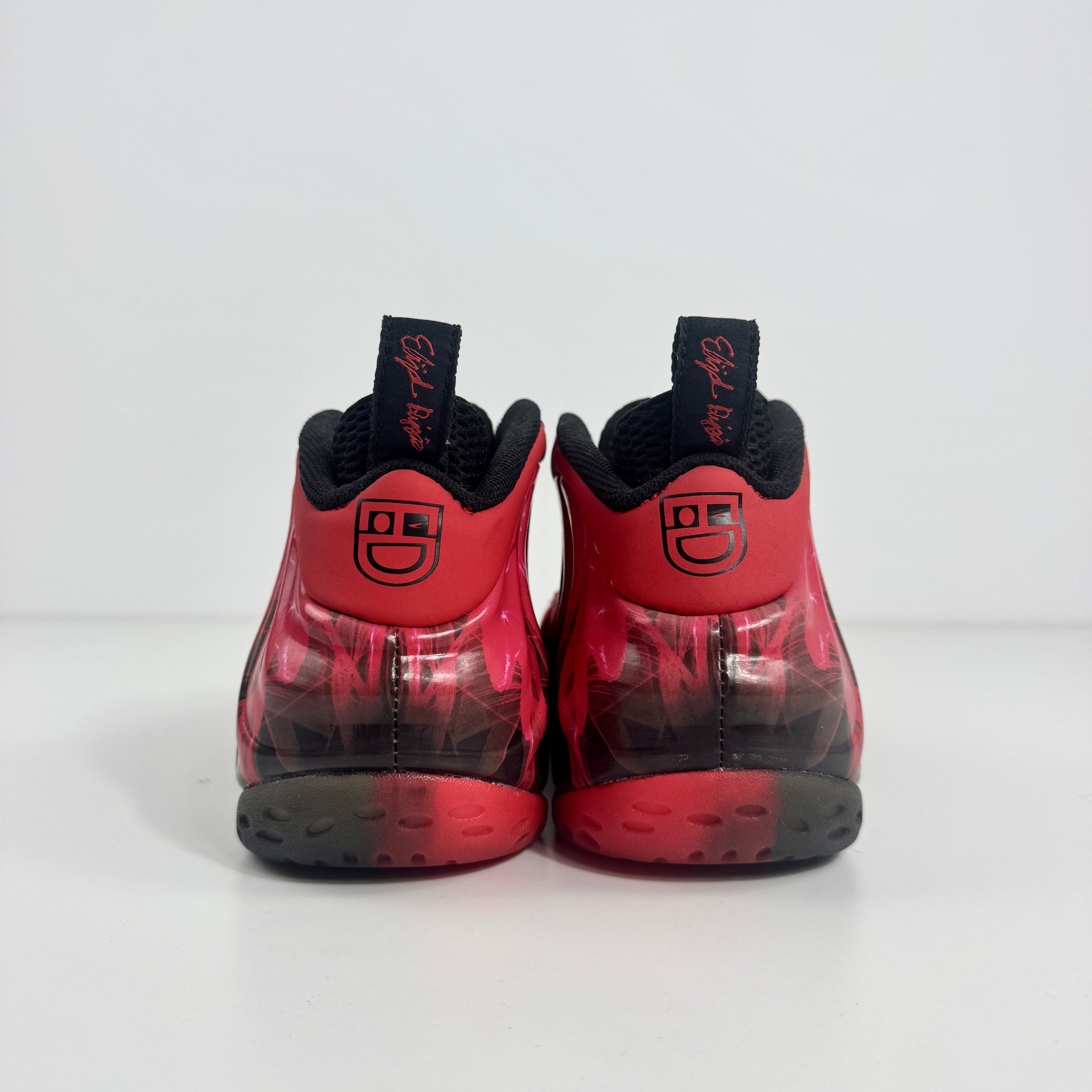 Nike Air Foamposite trainers in red and black with smiley faces on the heels, black pull tabs, and circular patterned soles.