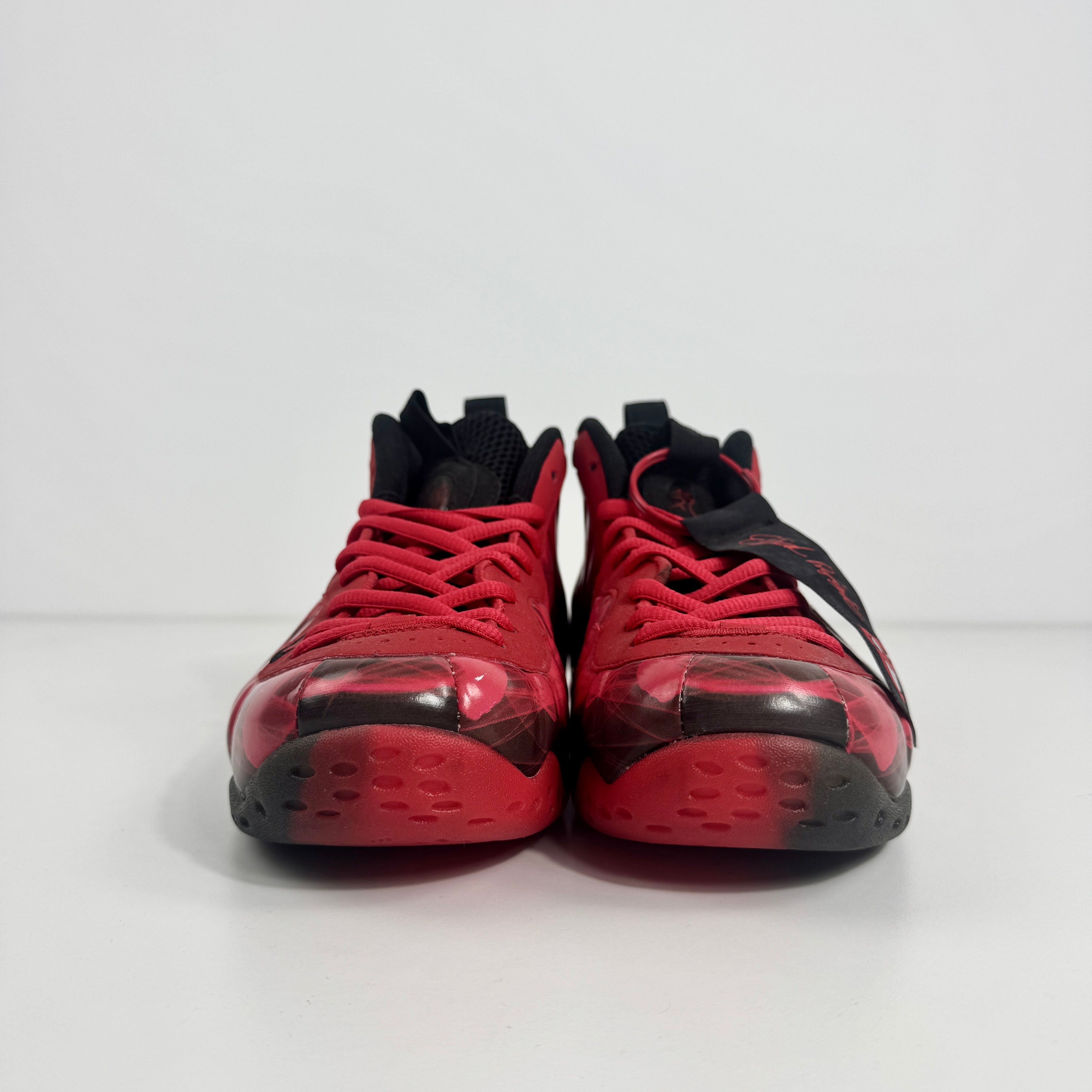 Nike Air Foamposite One trainers in red and black shown side by side on a white surface with a plain white background.