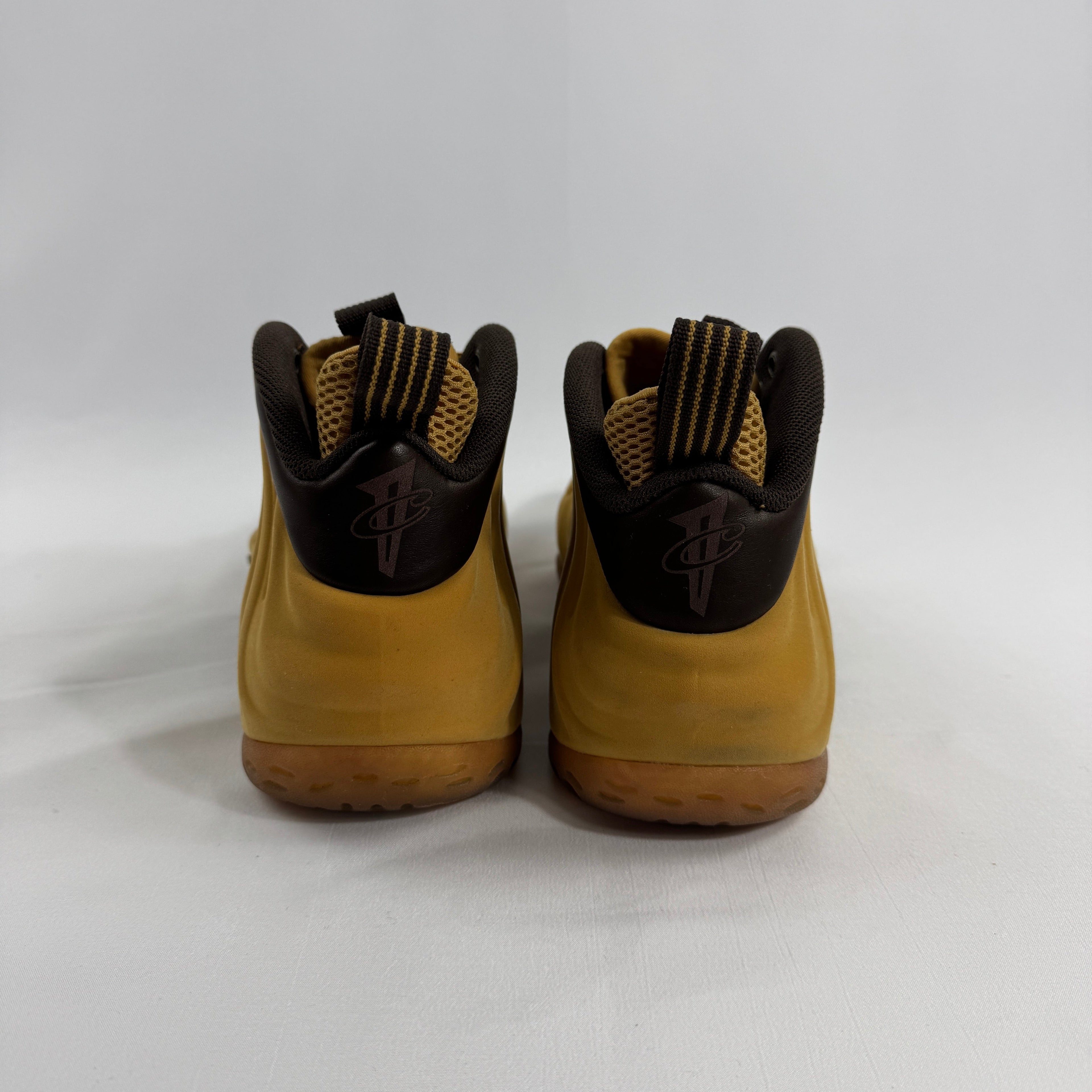 NIKE trainers in yellow and brown shown from the back with black heel logos and striped pull tabs, on a plain white background.