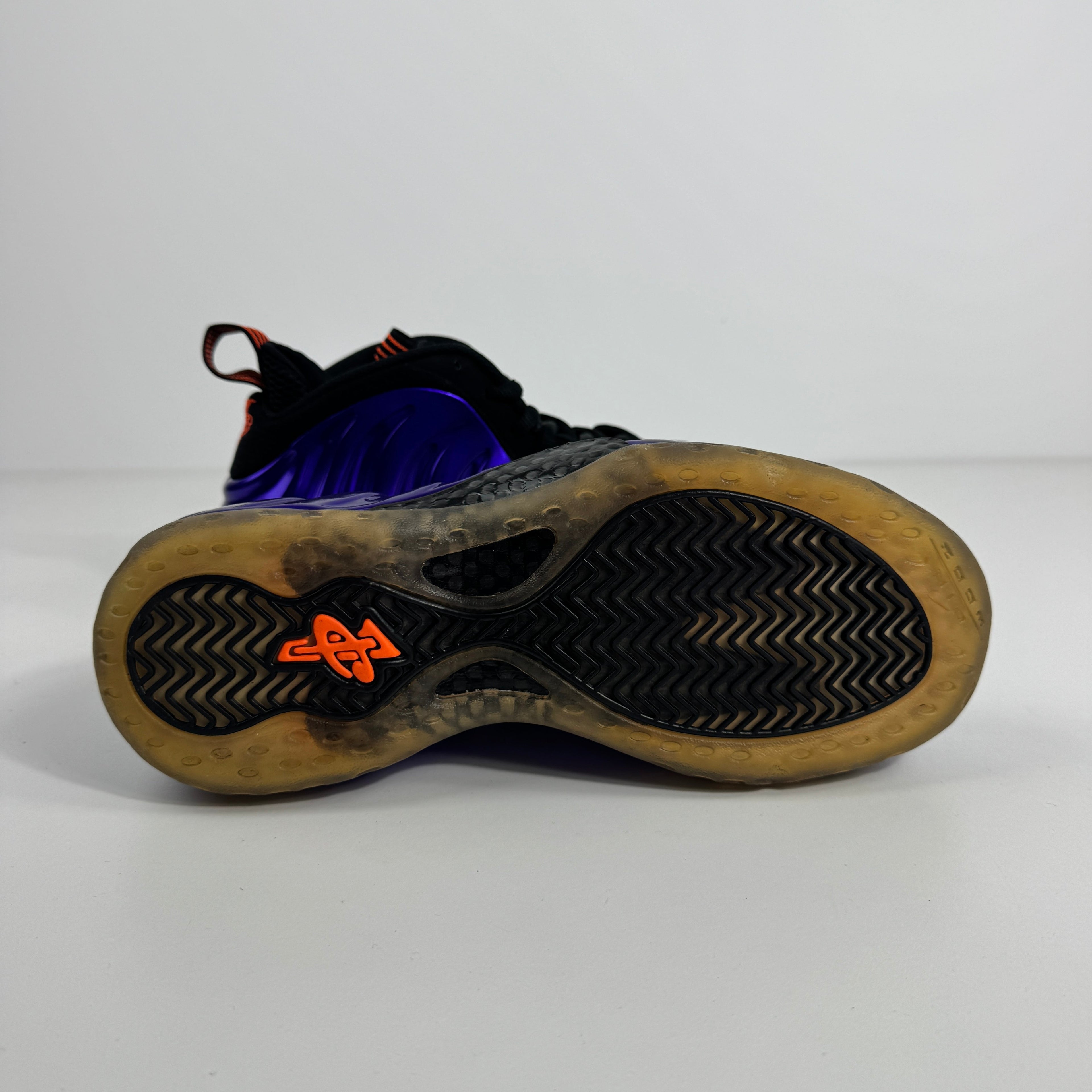 Nike Air Foamposite One trainer sole with translucent yellow grip, black herringbone tread, orange logo and black-blue upper accents.