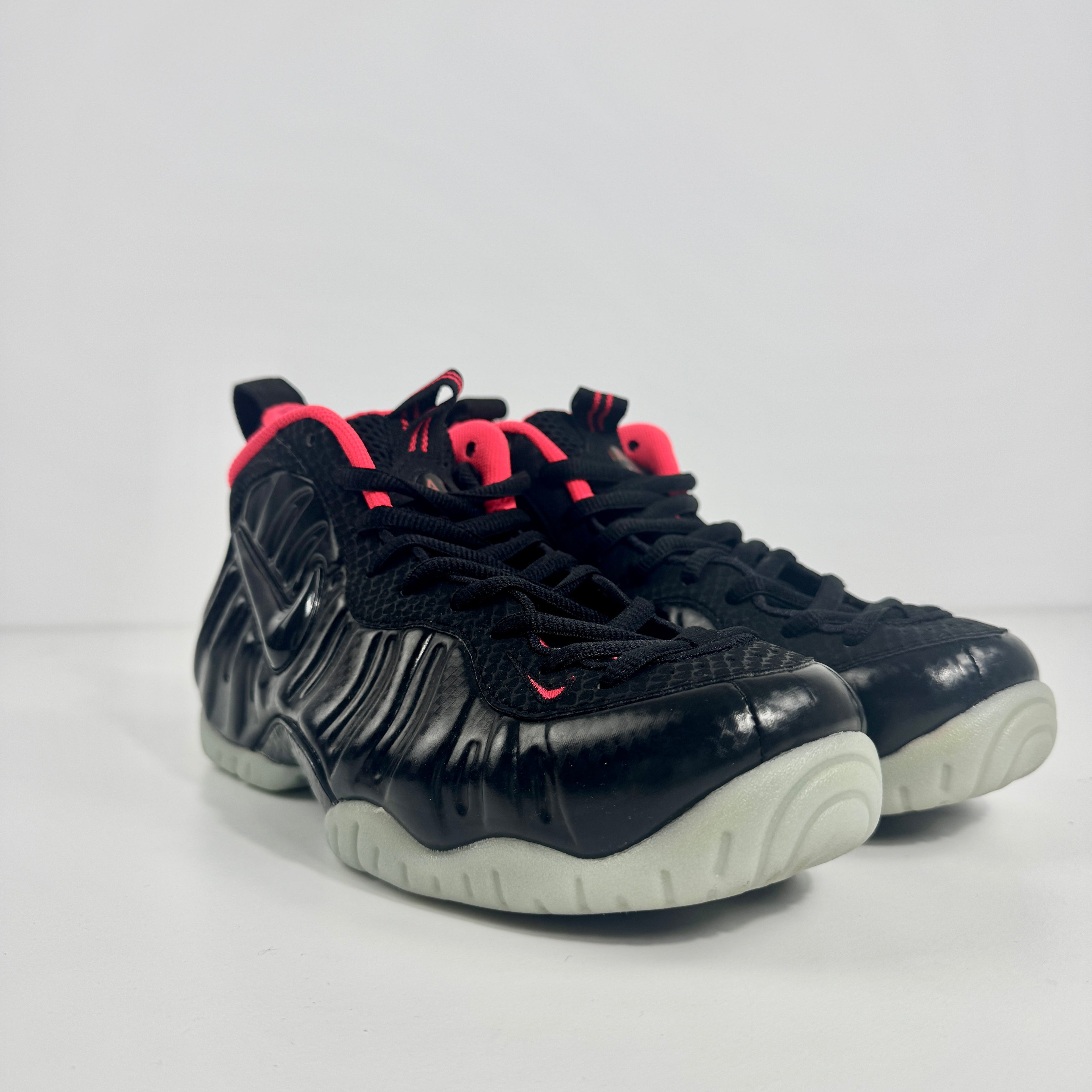 Nike trainers with a black moulded upper, wavy side texture, bright pink collar and tongue accents, and thick light grey soles on white background.