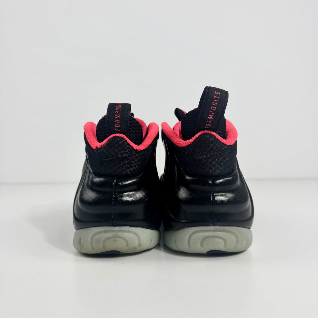 Back view of black Nike trainers with a pink inner lining, grey soles, and black pull tabs featuring red text, on a white background.