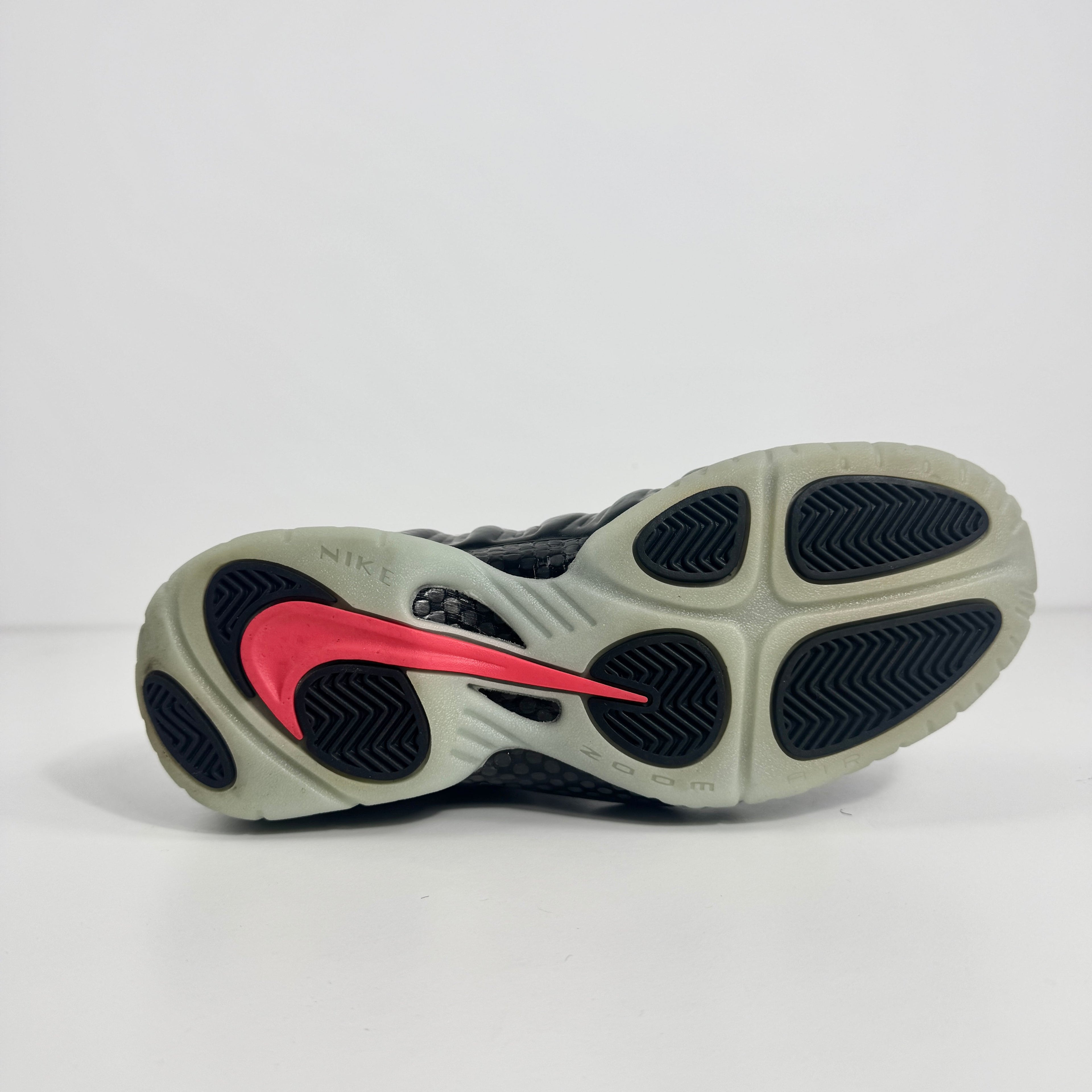 Sole of a Nike trainer with a red Swoosh, black tread detail, and cream accents on a white background.