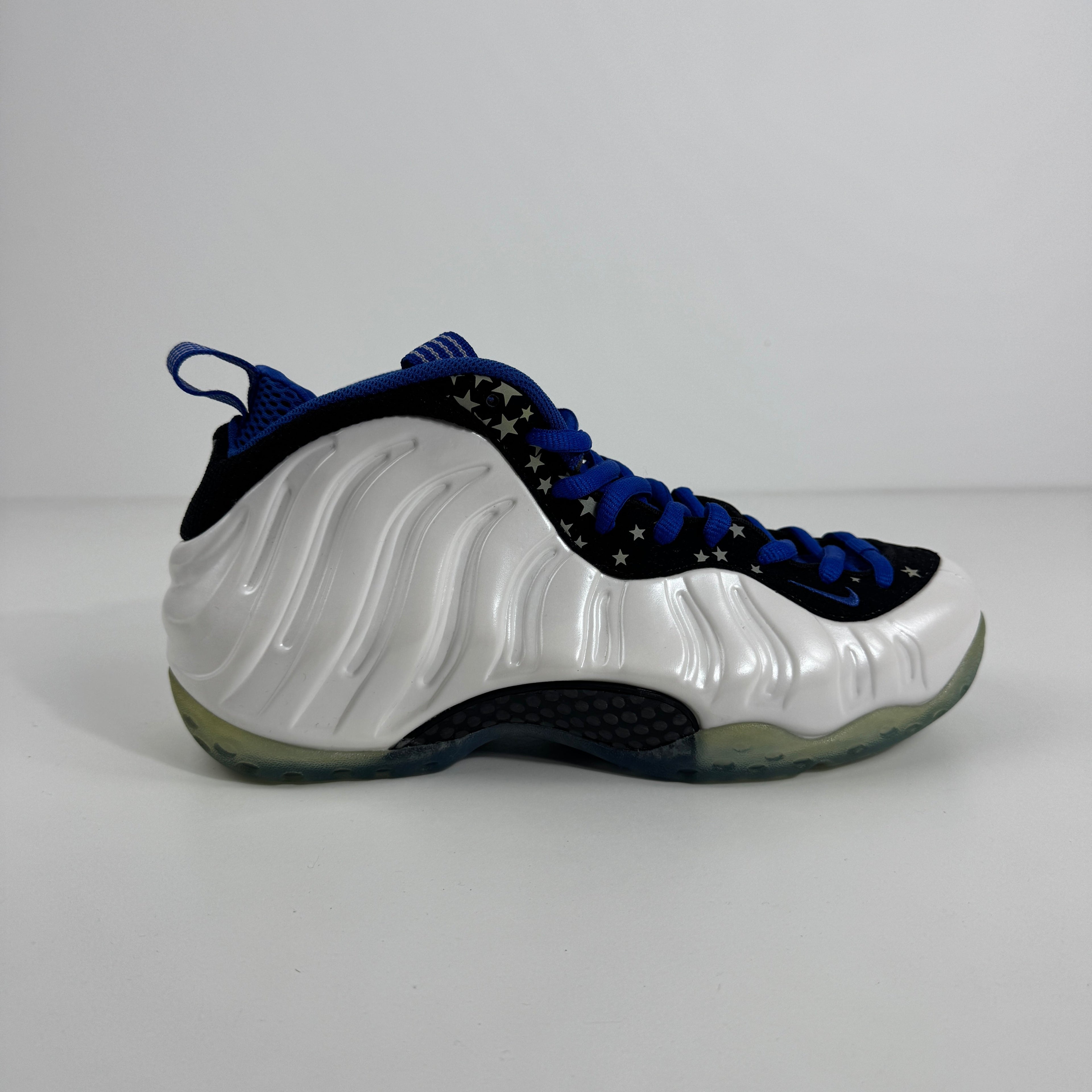 Nike trainers with a glossy white wavy shell, black upper decorated with white stars, blue laces, and a semi-translucent sole on white background.