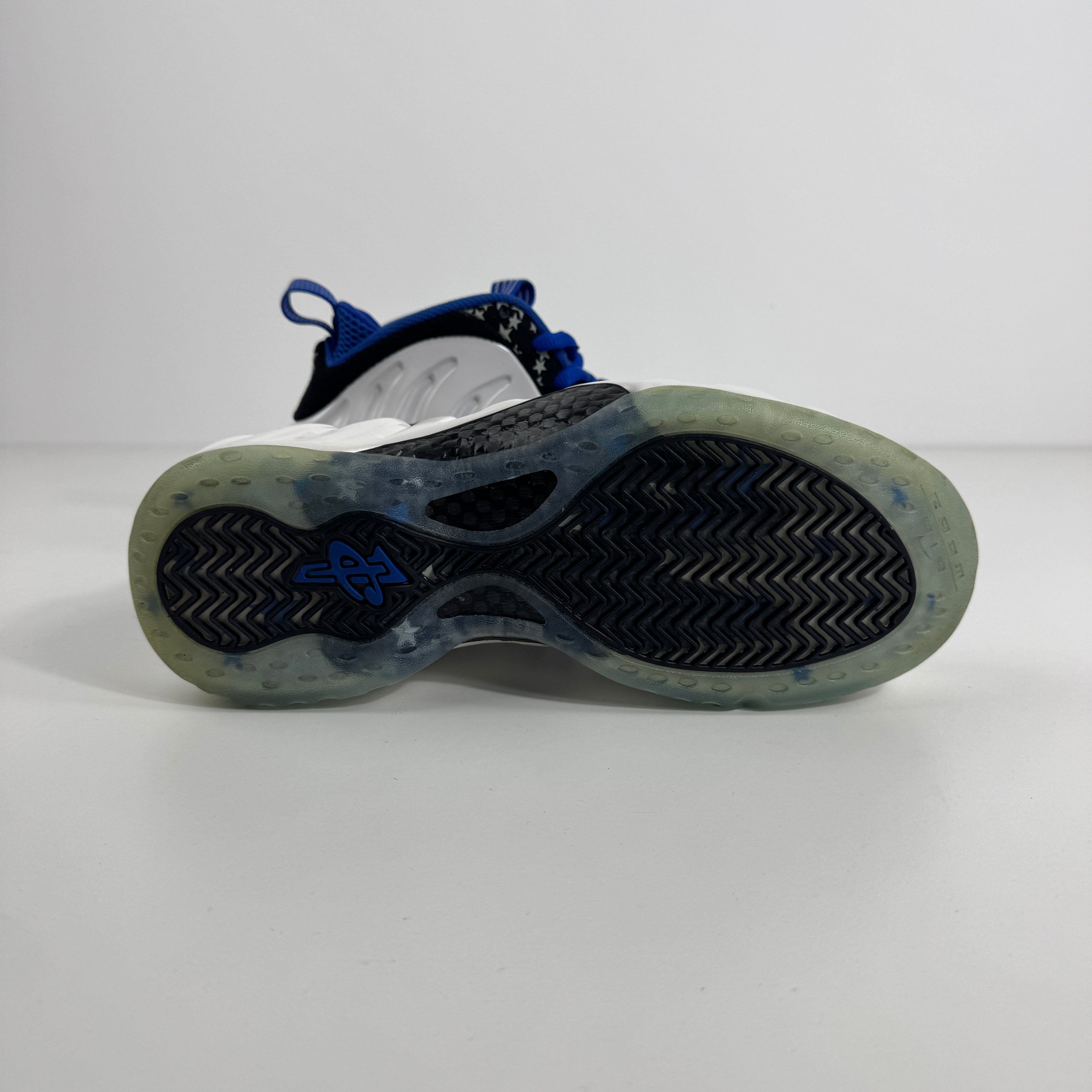 Close-up of a Nike trainer outsole with a translucent base, black herringbone grip, and blue details on a plain white background.