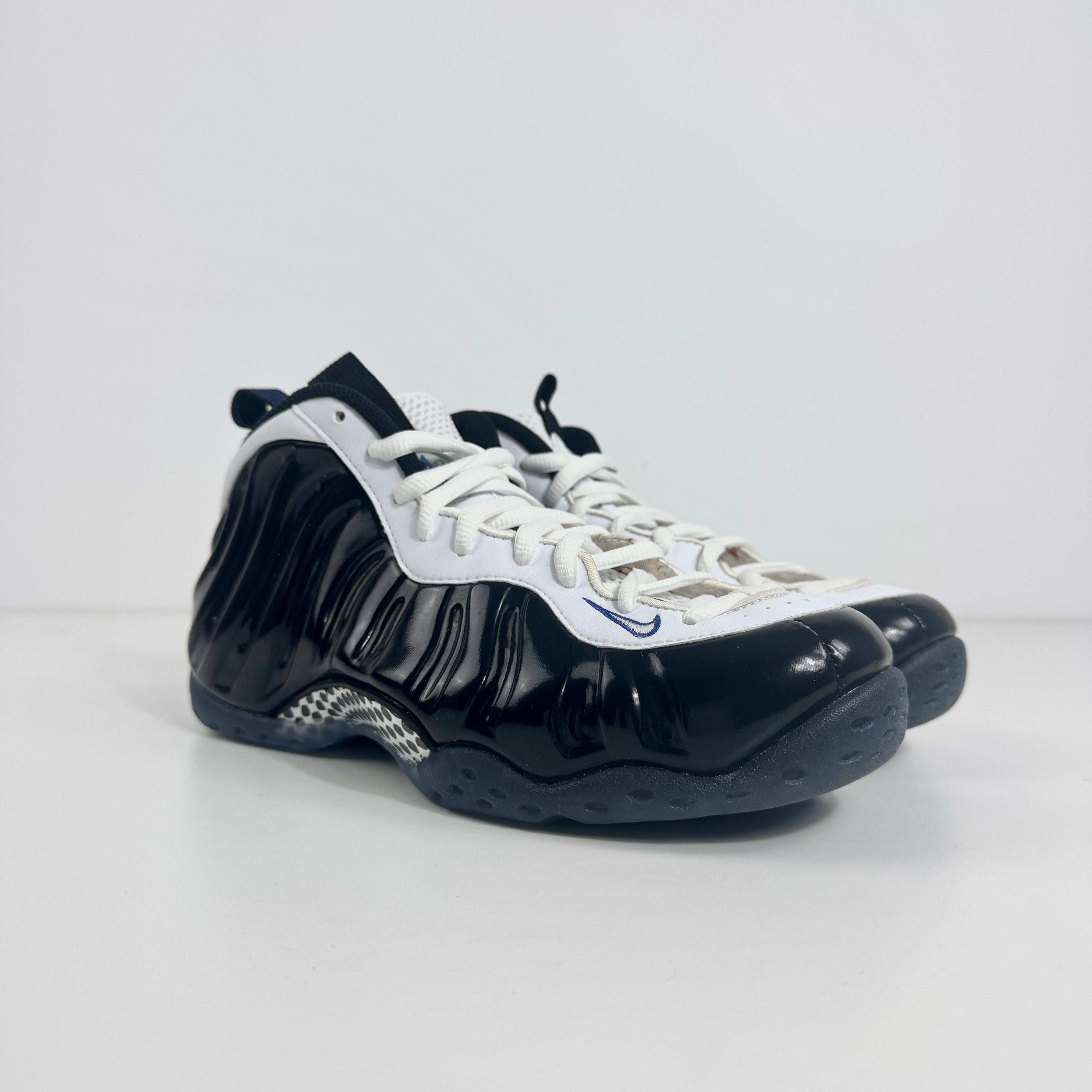 The Nike Air Foamposite One Concord UK 7 features a shiny black molded upper paired with stark white leather trim along the