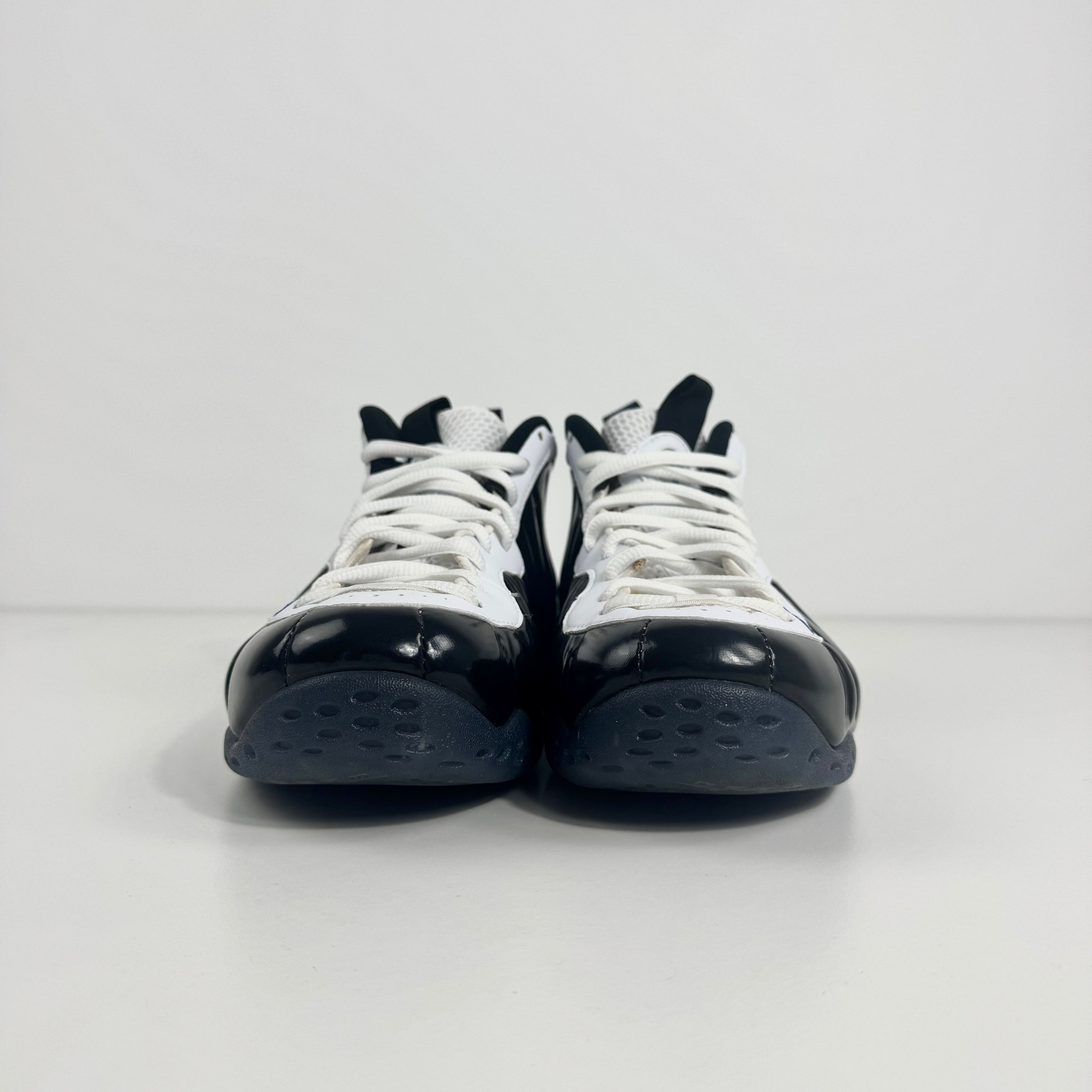 The Nike Air Foamposite One Concord UK 7 features a shiny black molded upper paired with stark white leather trim along the
