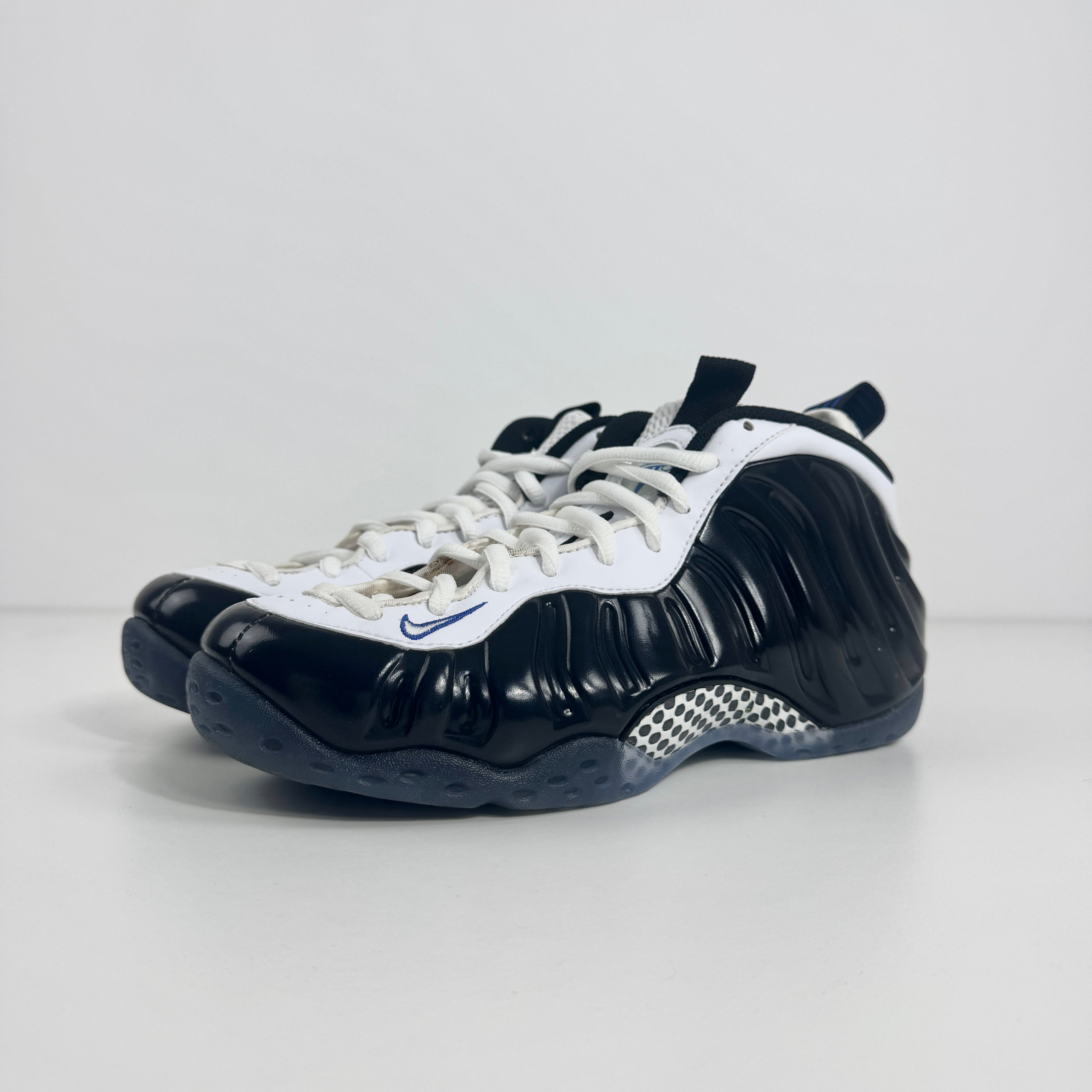 The Nike Air Foamposite One Concord UK 7 features a shiny black molded upper paired with stark white leather trim along the