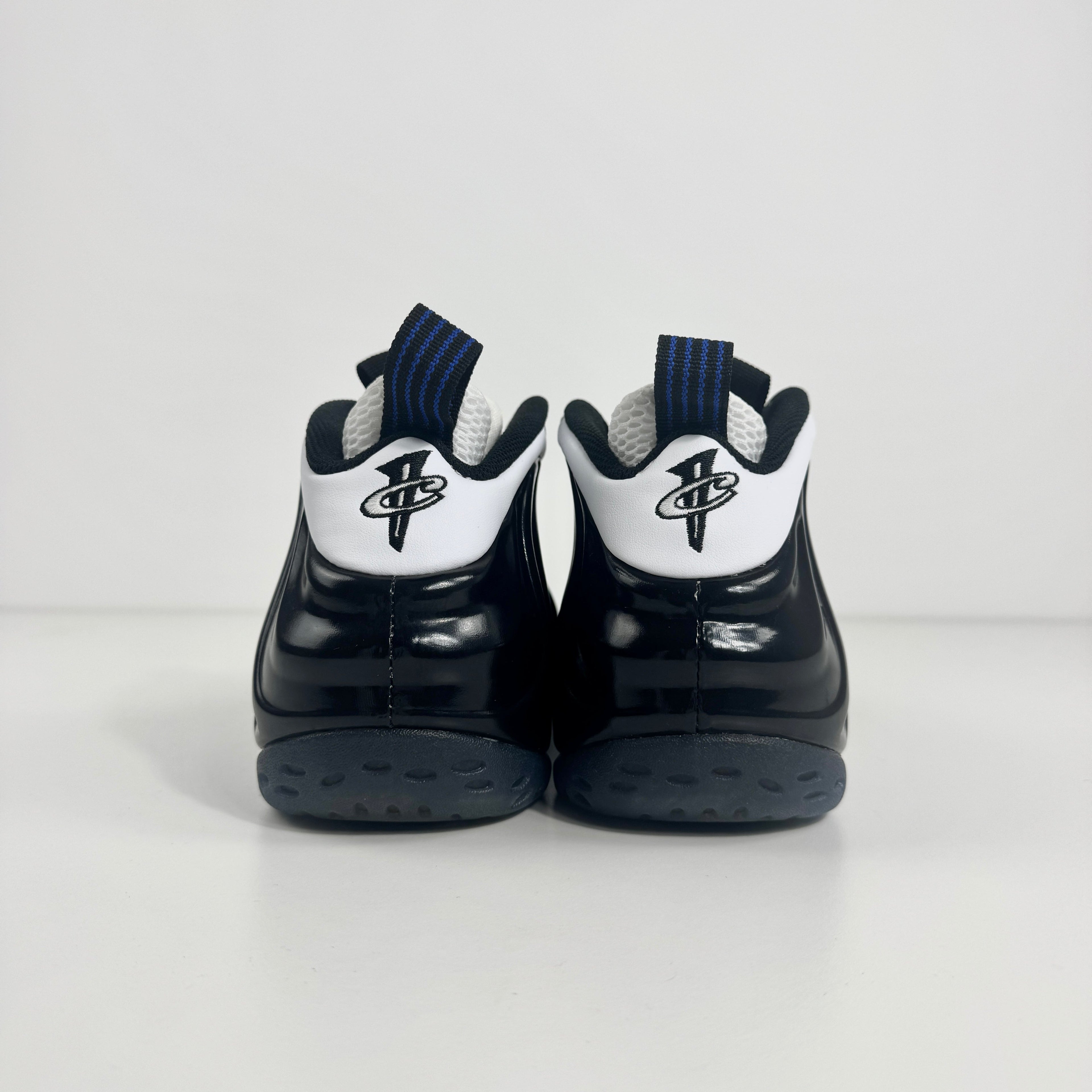 The Nike Air Foamposite One Concord UK 7 features a shiny black molded upper paired with stark white leather trim along the