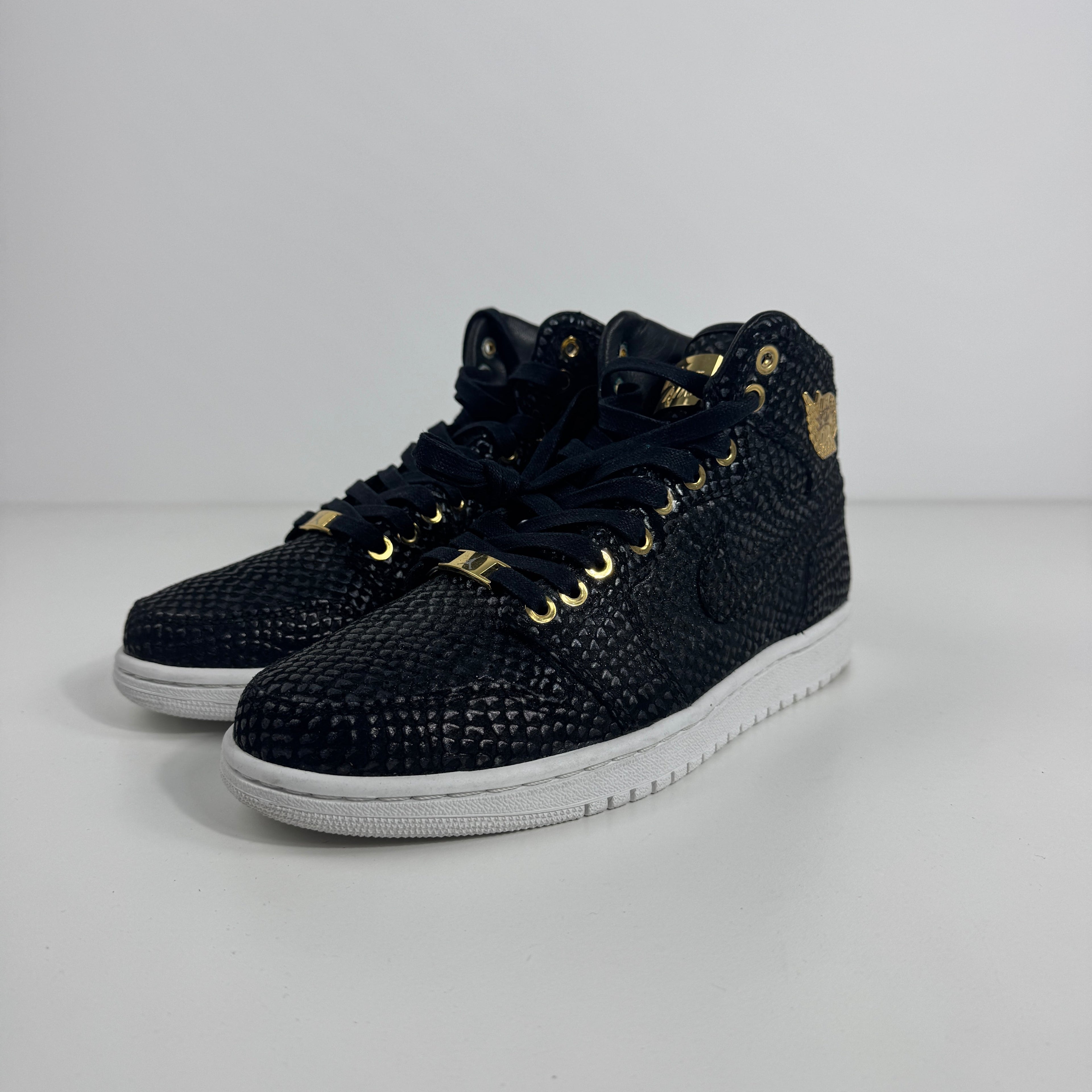Nike Air Jordan 1 Pinnacle trainers in black textured material with gold accents, black laces and white soles on a white background.