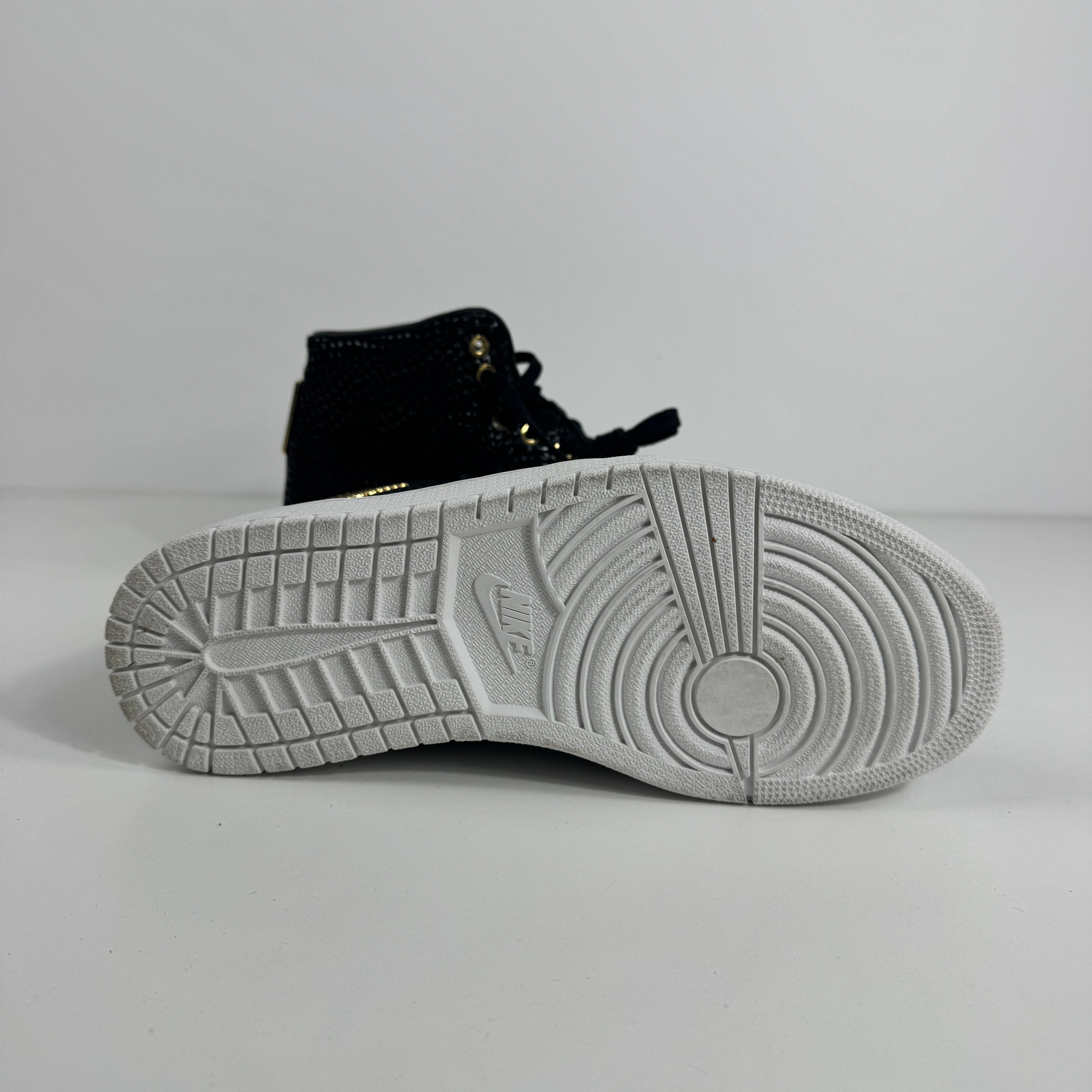 Black NIKE Air Jordan 1 trainer shown side-on, highlighting the white sole with circular and linear treads on a plain background.