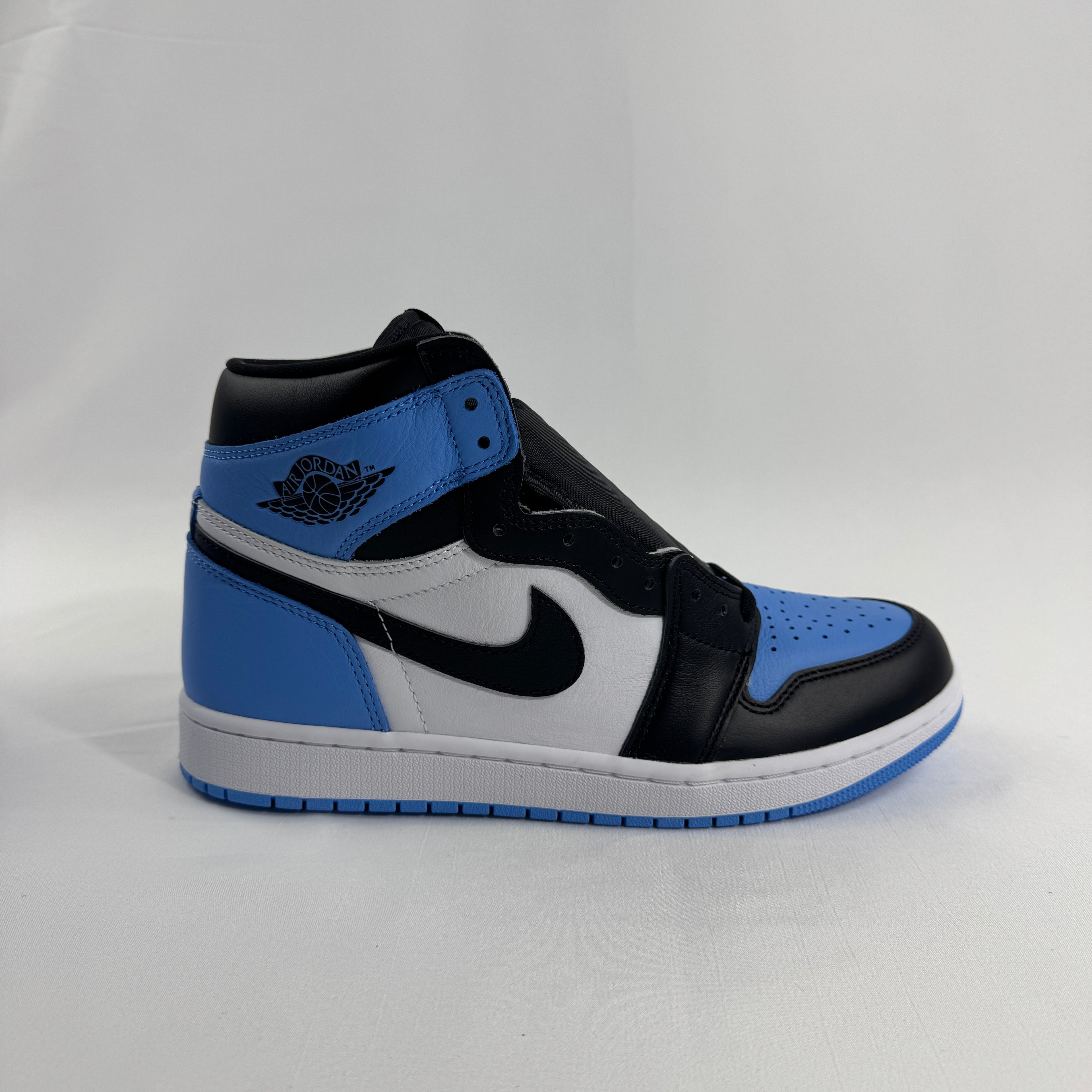 A Nike high-top trainer in black, white and light blue with a black Swoosh and Air Jordan logo, shown on a white surface.