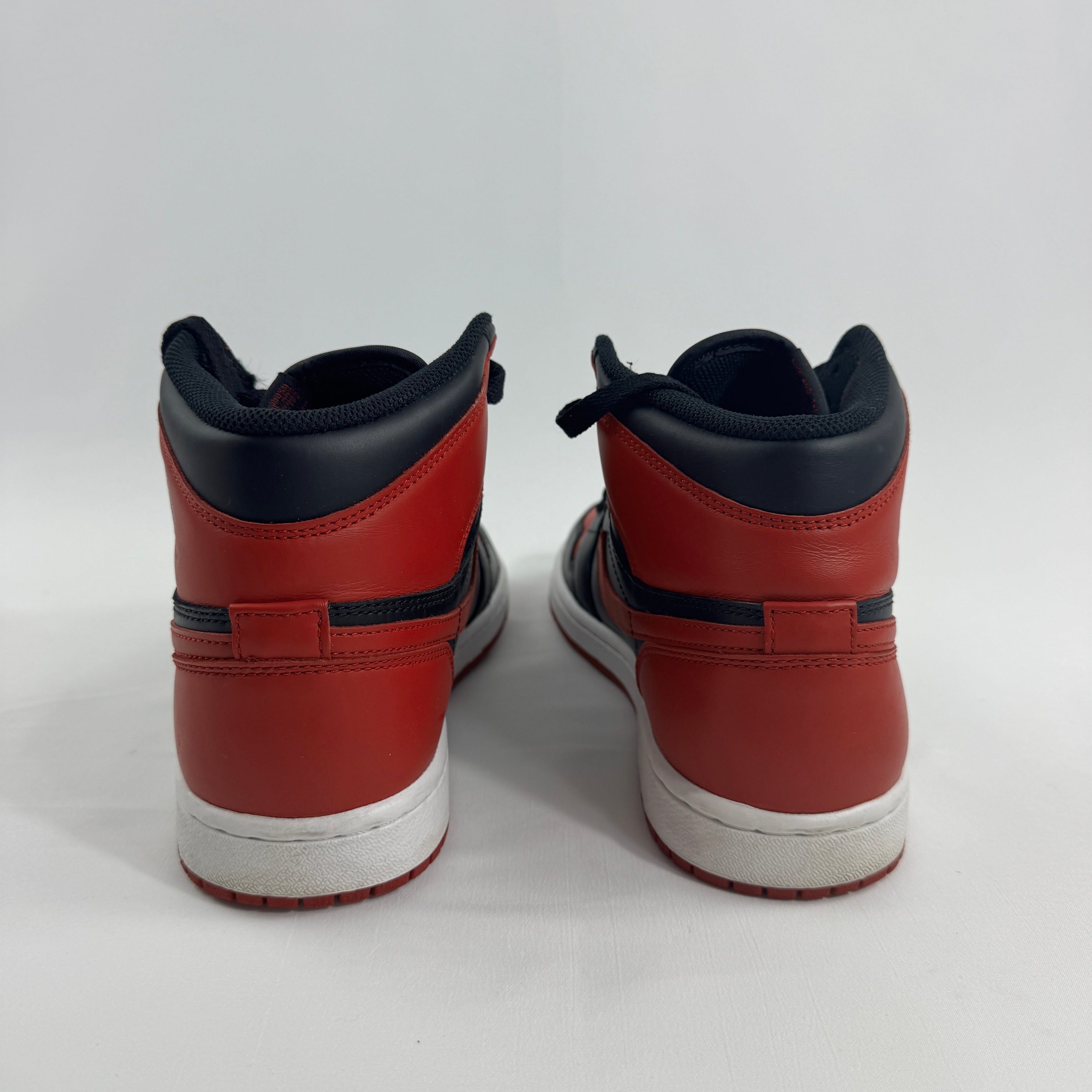 Pair of NIKE Air Jordan 1 trainers in red, black and white leather, shown from the back on a white surface with plain background.