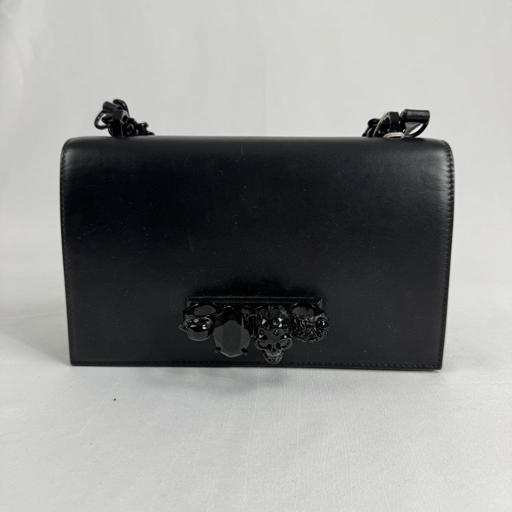The Alexander McQueen Blackout Leather Crossbody Knuckle Bag is a bold statement piece featuring smooth black leather, a