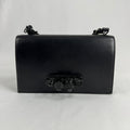 The Alexander McQueen Blackout Leather Crossbody Knuckle Bag is a bold statement piece featuring smooth black leather, a
