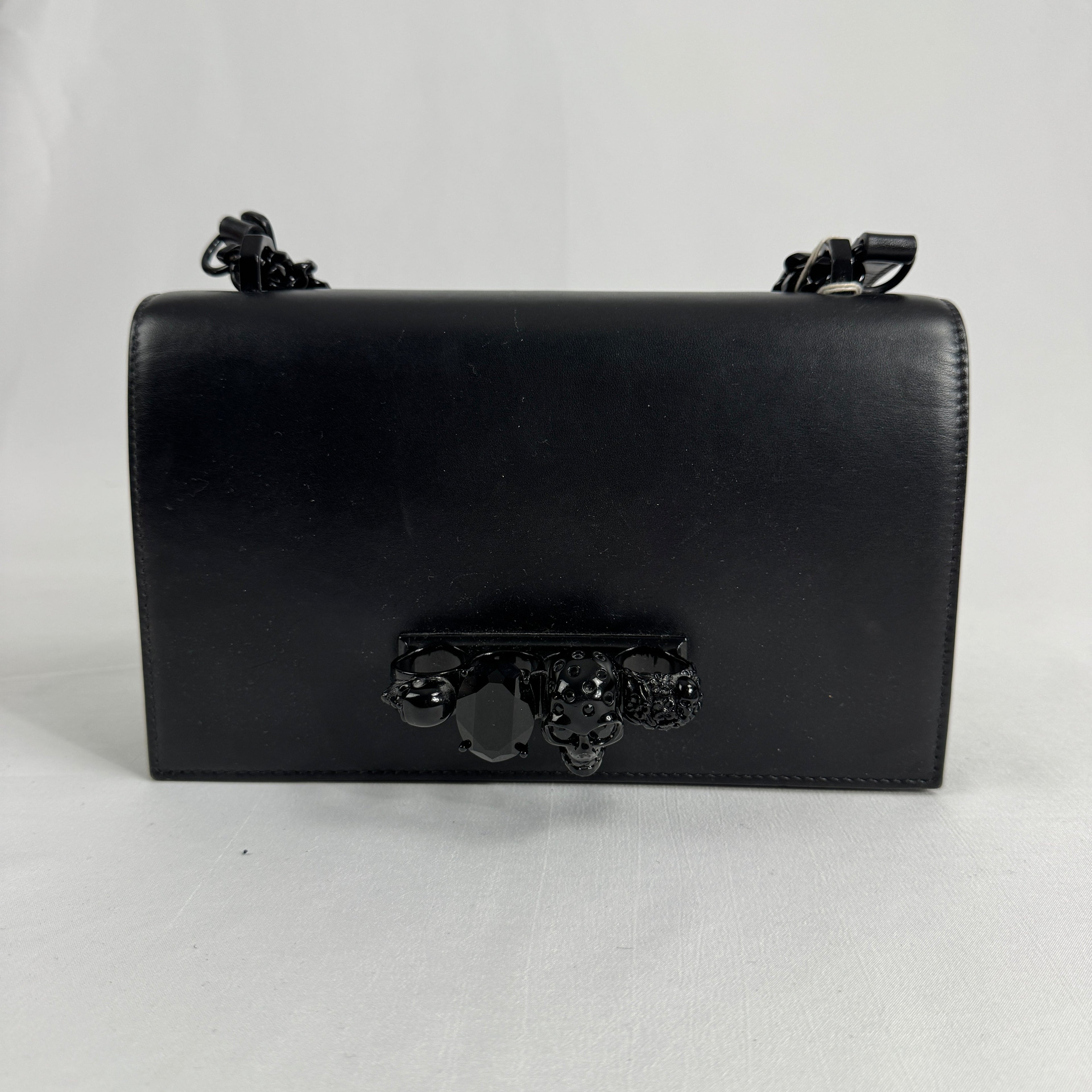 The Alexander McQueen Blackout Leather Crossbody Knuckle Bag is a bold statement piece featuring smooth black leather, a