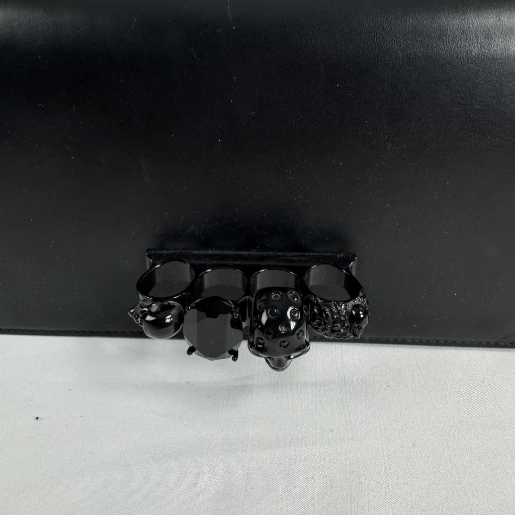 The Alexander McQueen Blackout Leather Crossbody Knuckle Bag is a bold statement piece featuring smooth black leather, a