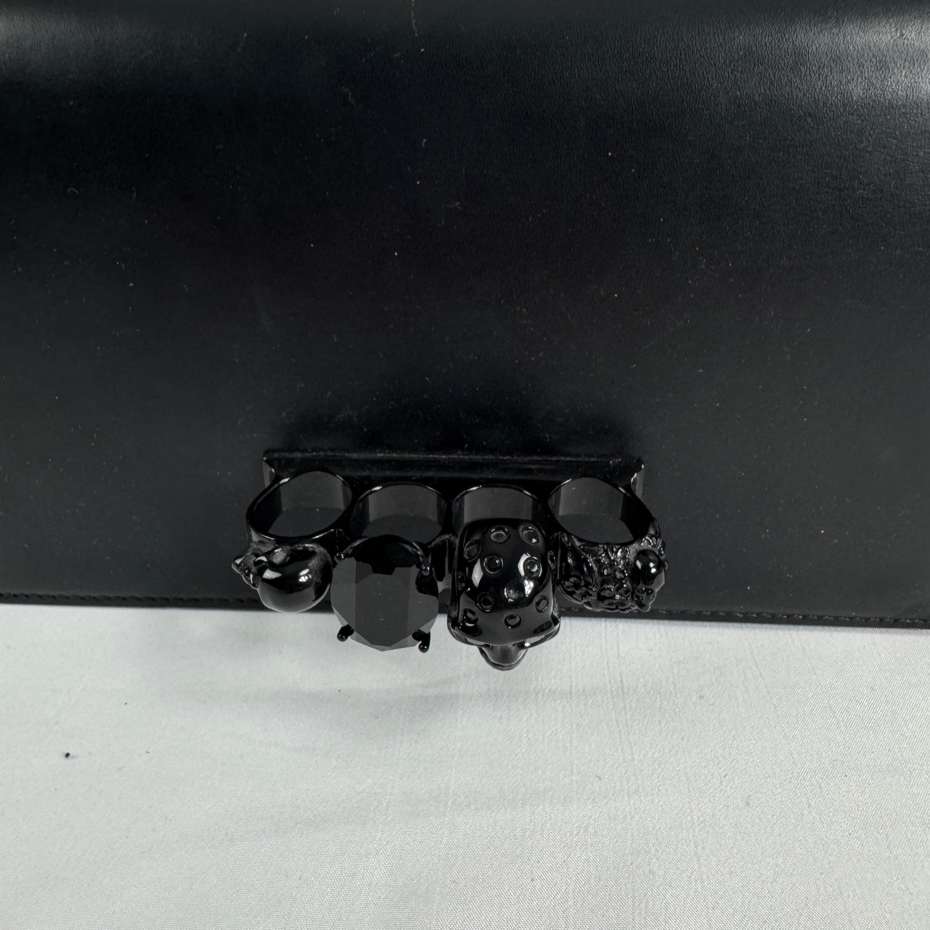The Alexander McQueen Blackout Leather Crossbody Knuckle Bag is a bold statement piece featuring smooth black leather, a