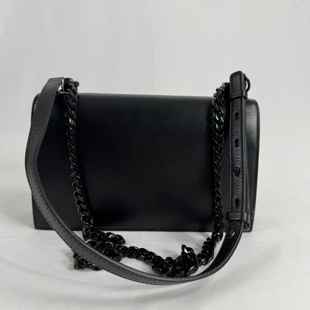 The Alexander McQueen Blackout Leather Crossbody Knuckle Bag is a bold statement piece featuring smooth black leather, a