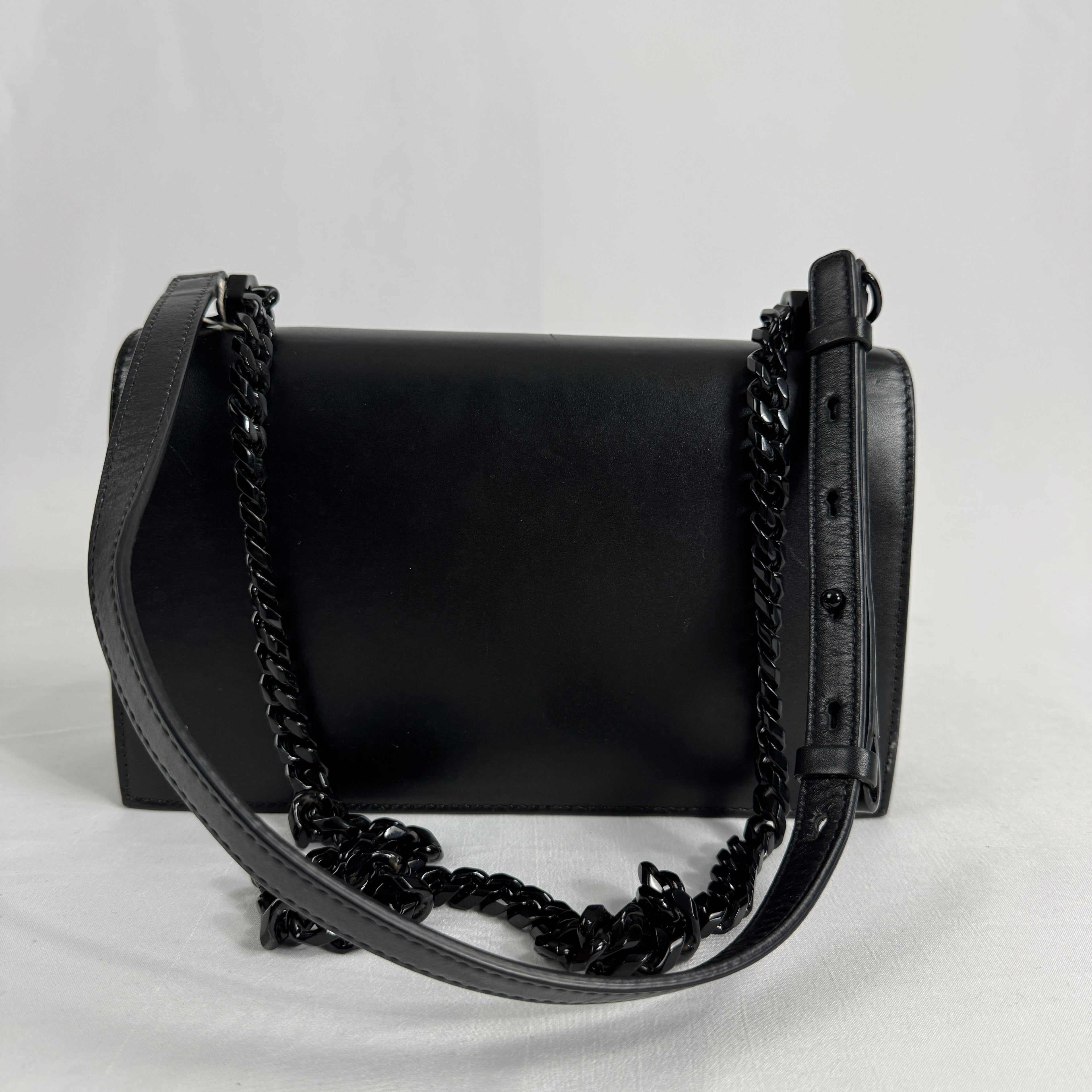 The Alexander McQueen Blackout Leather Crossbody Knuckle Bag is a bold statement piece featuring smooth black leather, a