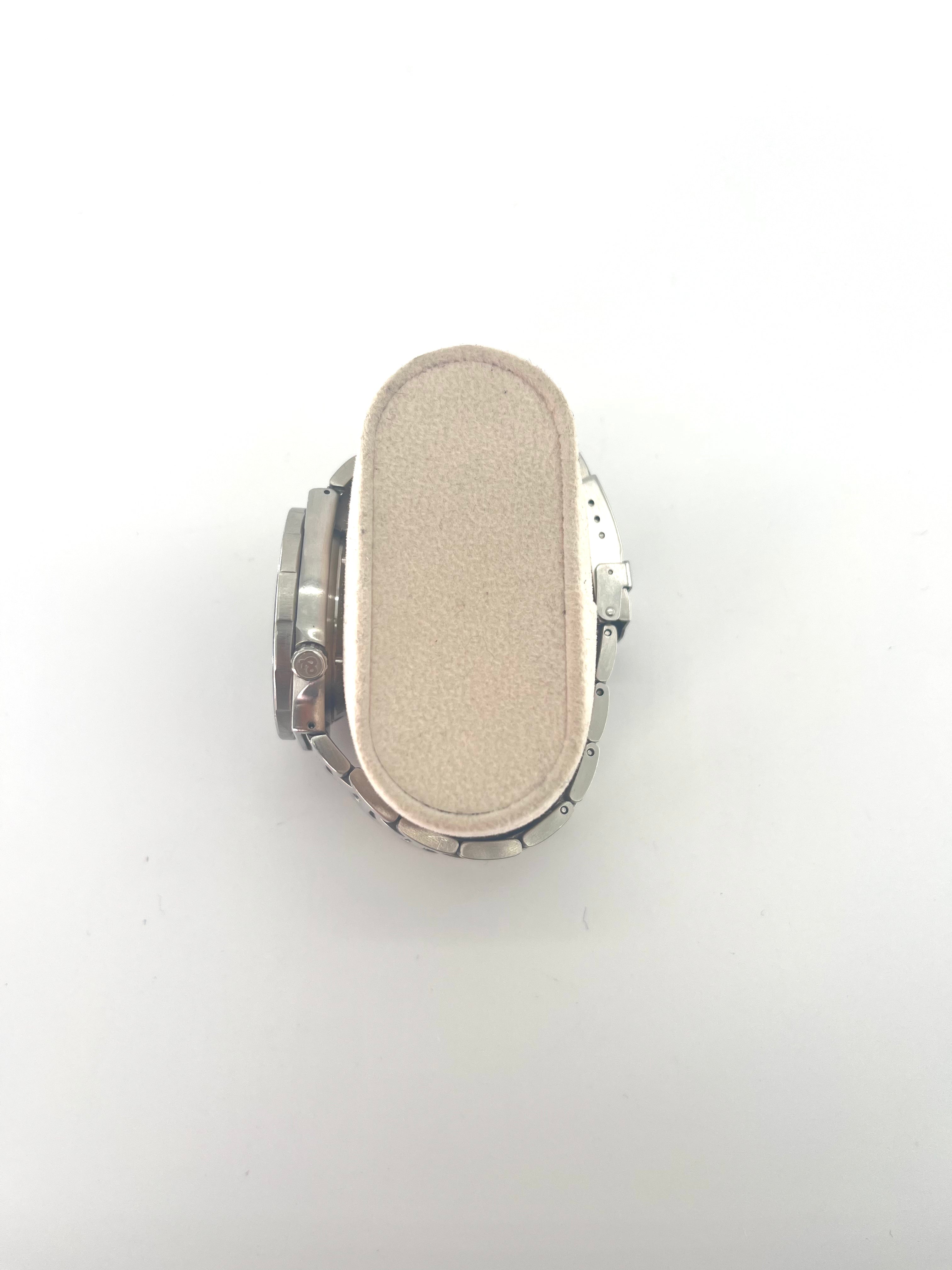 A Bell and Ross silver wristwatch with a round face is displayed on a beige cushion, shown with additional interchangeable straps.