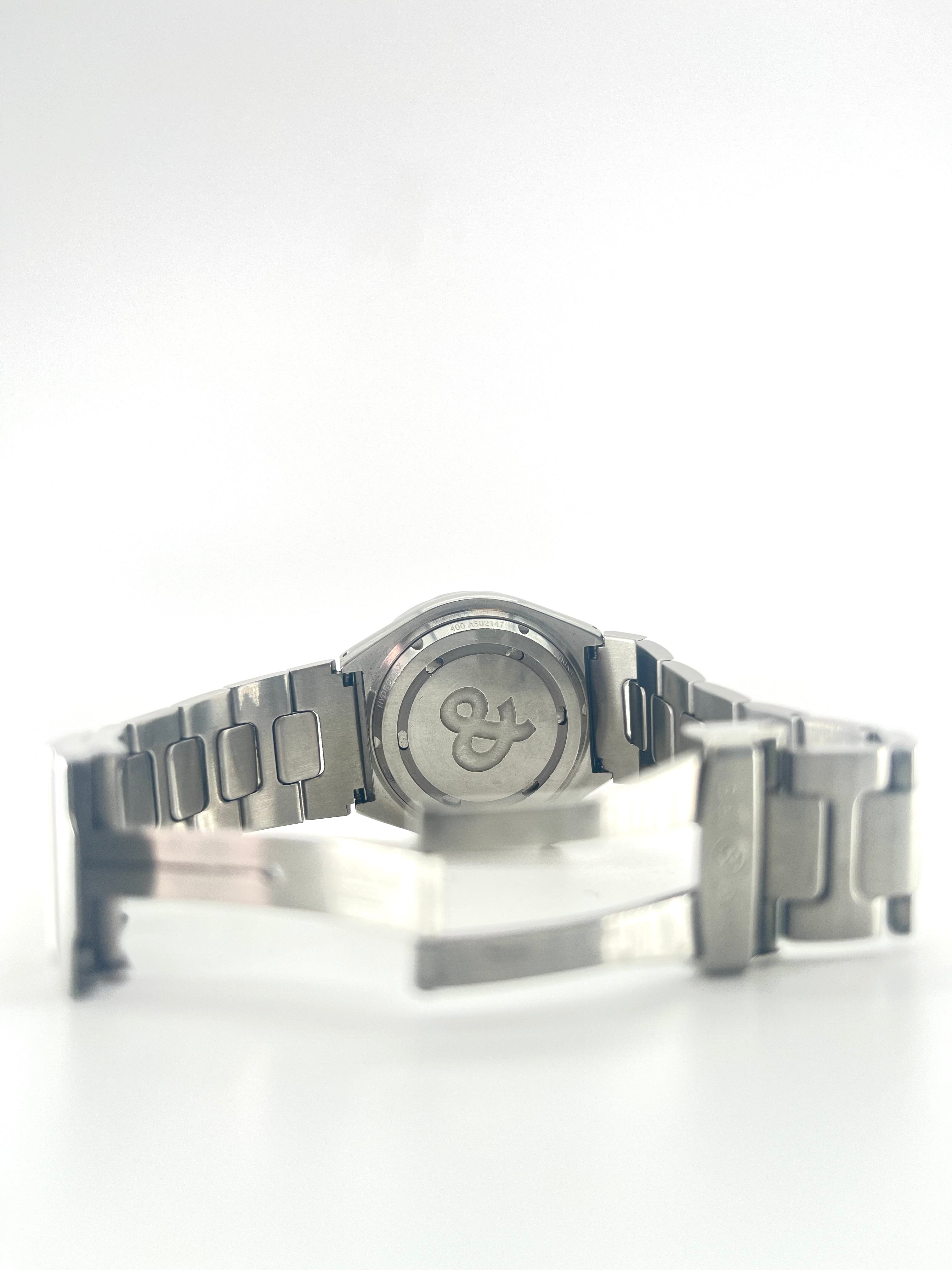 Rear view of a Bell and Ross silver metal wristwatch with an open clasp and extra straps placed beside it on a white background.