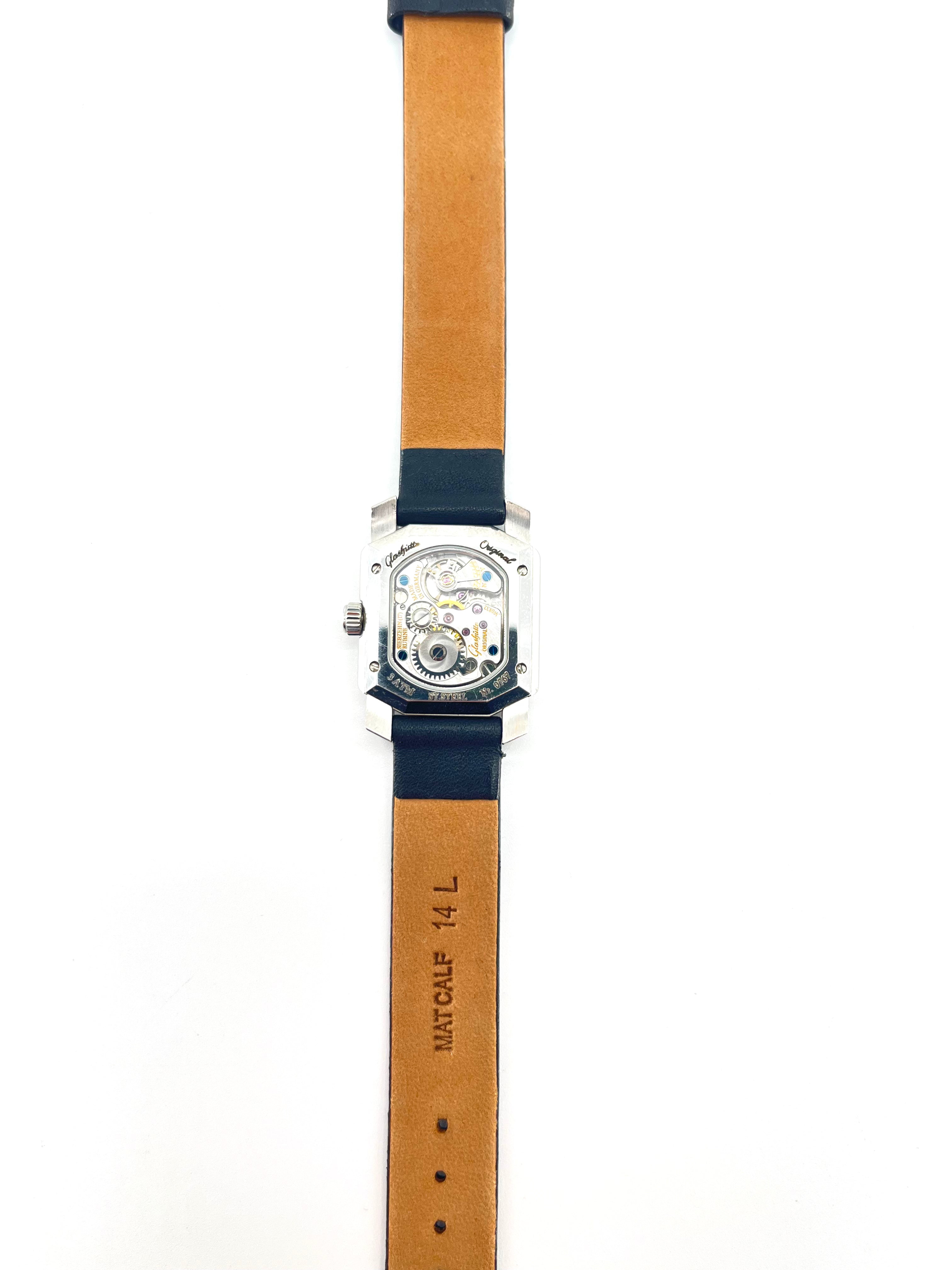 Glashutte Origin Lady Karree watch with a tan leather strap, rectangular silver case, diamond details and exposed movement.