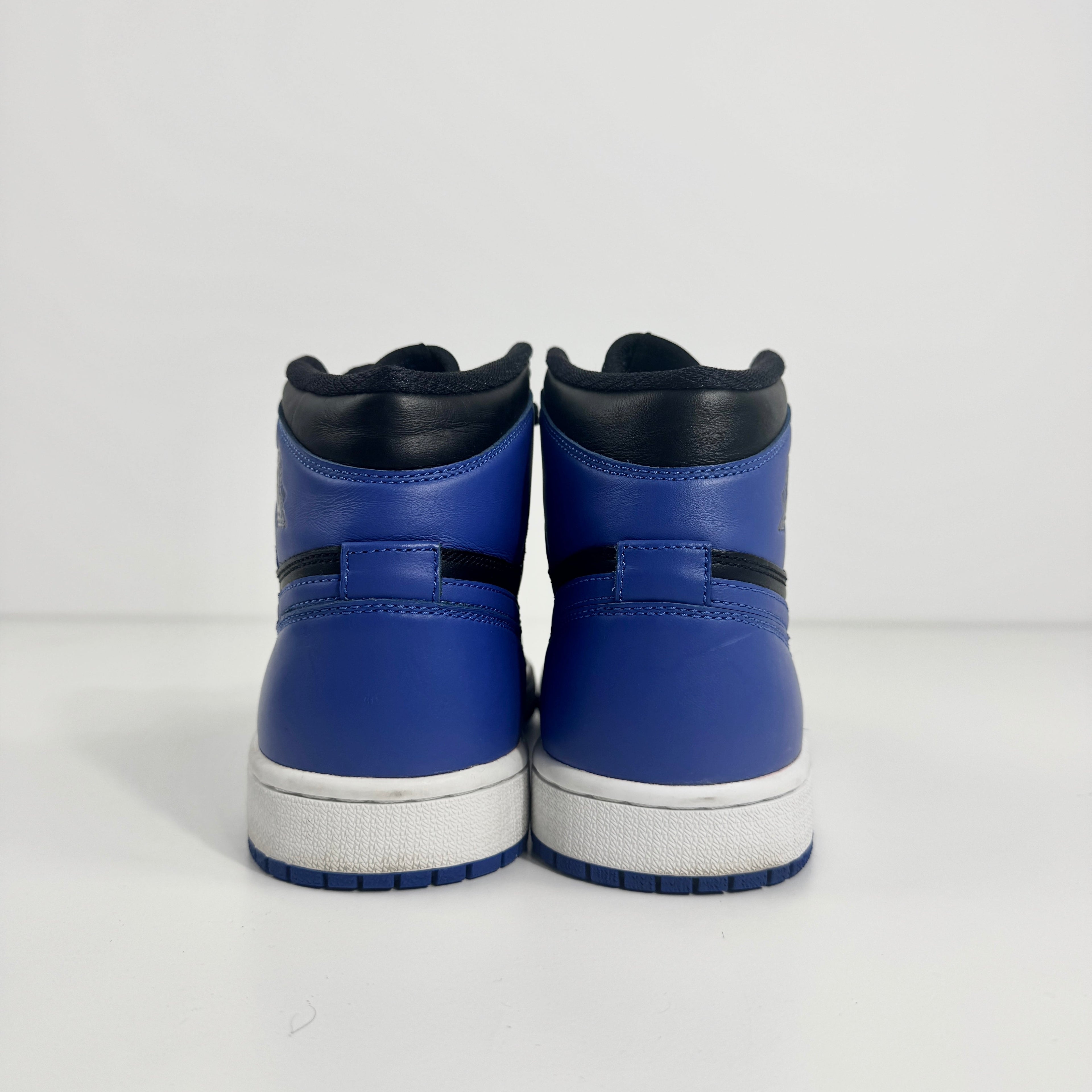 A pair of Jordan 1 Retro high-top trainers in black and royal blue, shown from the back against a plain white background.