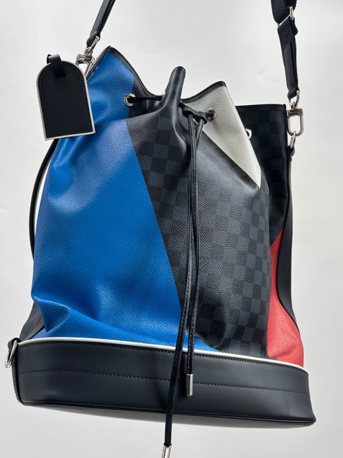 Louis Vuitton bucket bag with blue, red, black and grey check panels, black strap, silver hardware and drawstring on white background.