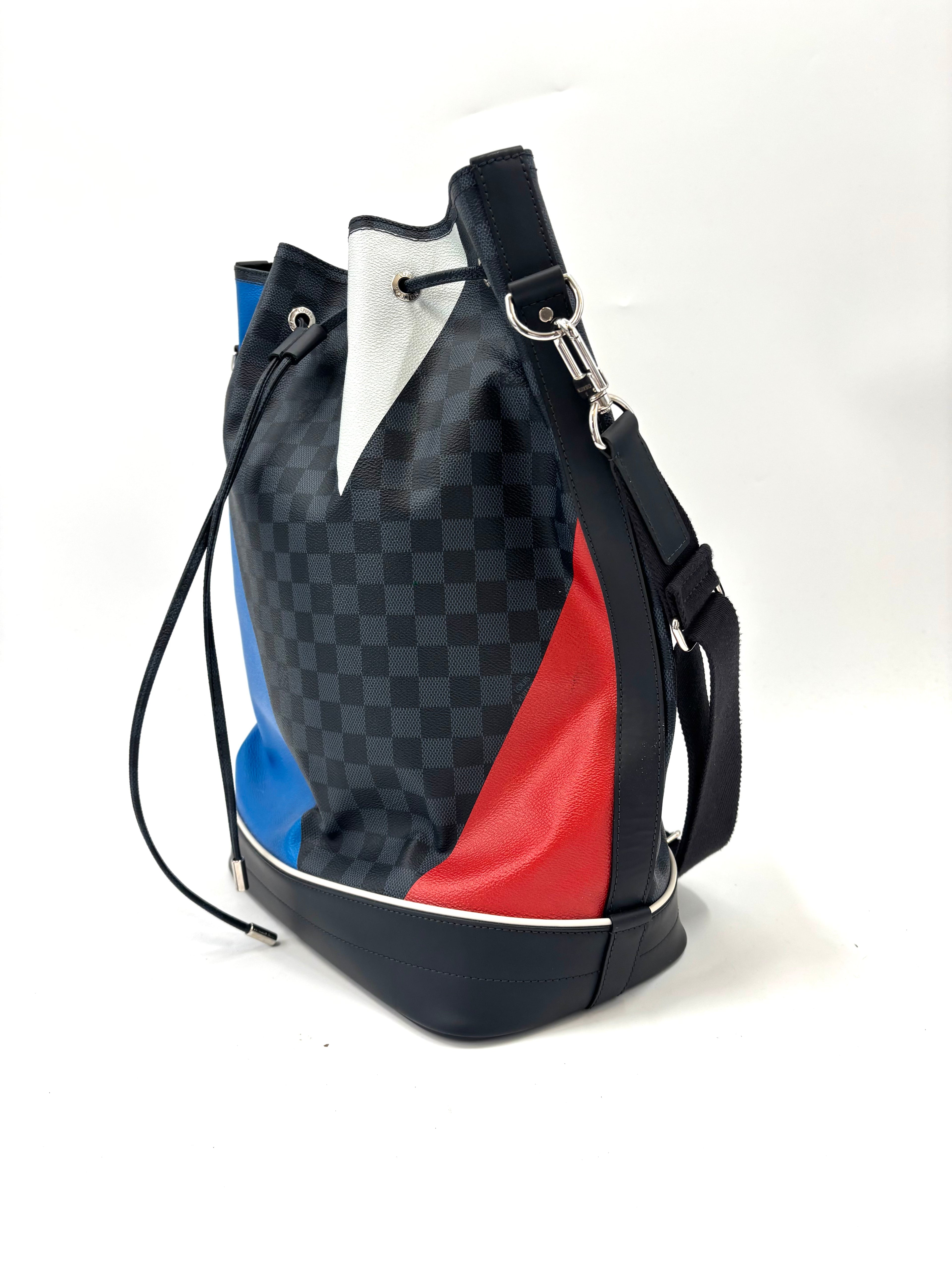 Louis Vuitton bucket bag with a black check pattern, blue, red and white details, silver hardware and a shoulder strap on white background.
