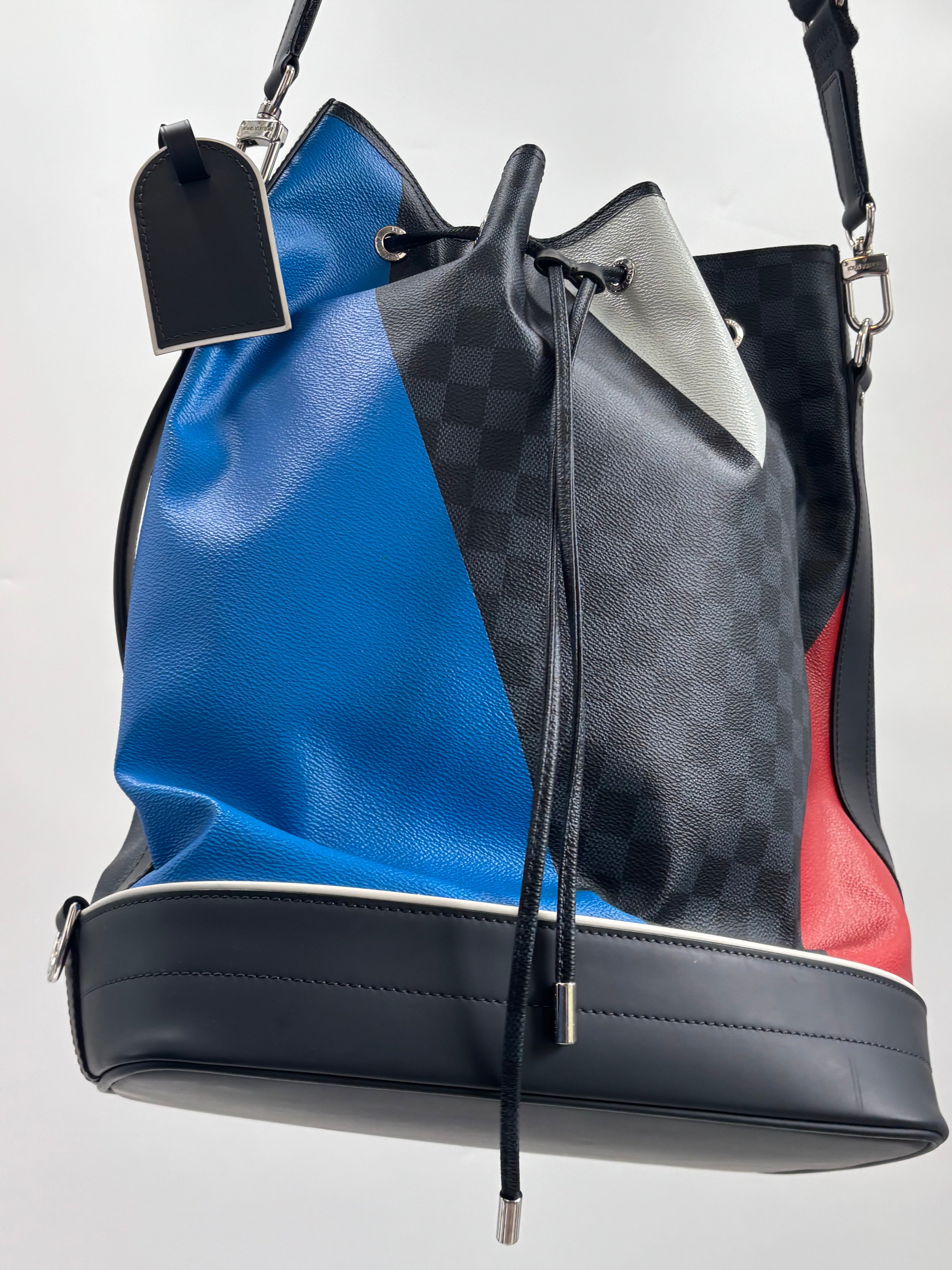 Louis Vuitton bucket bag in blue and black checkered leather with red and grey panels, black straps, on a white background.