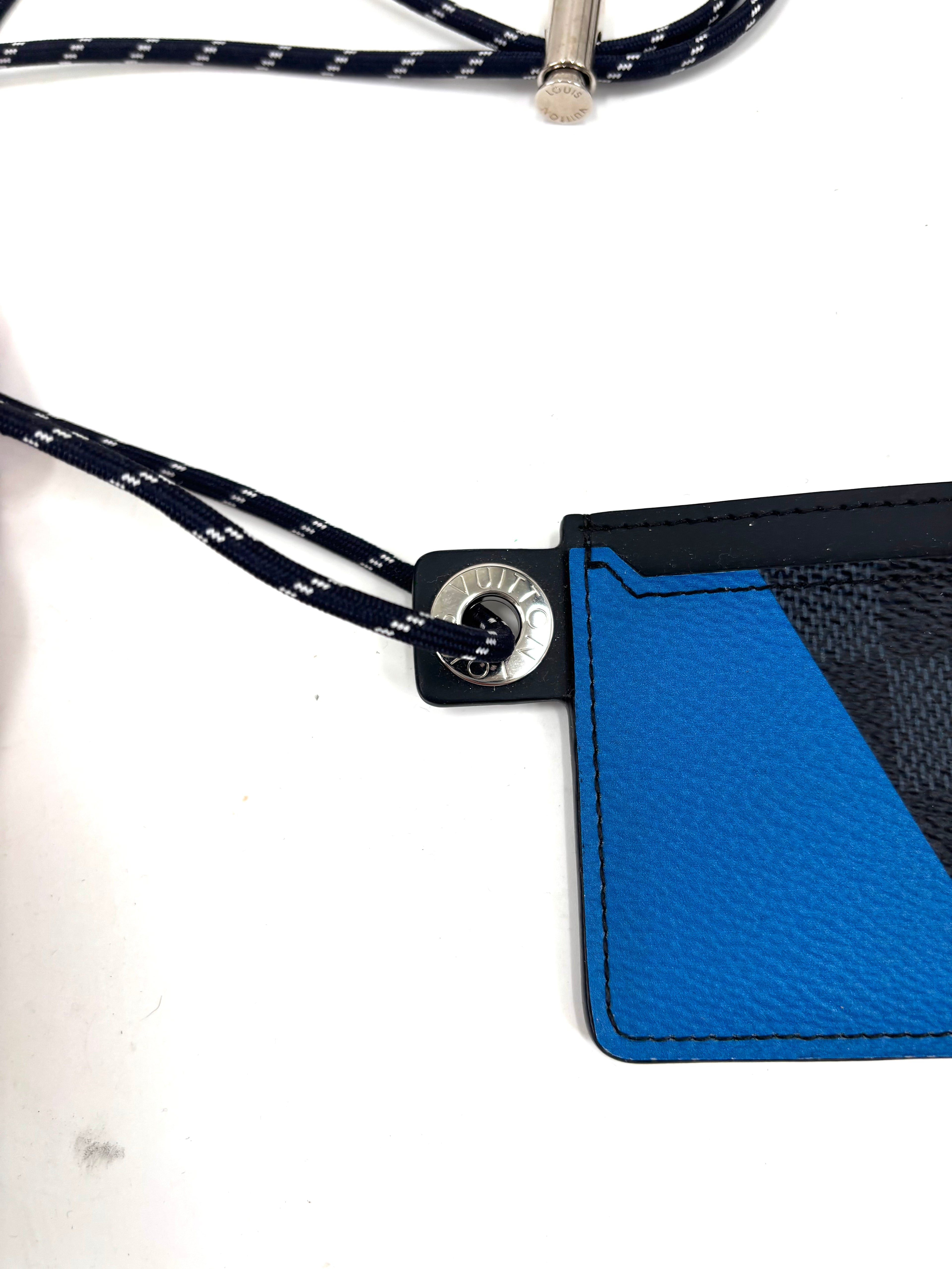 Close-up of a Louis Vuitton card holder in blue leather with a black and blue cord through a silver grommet on the corner.