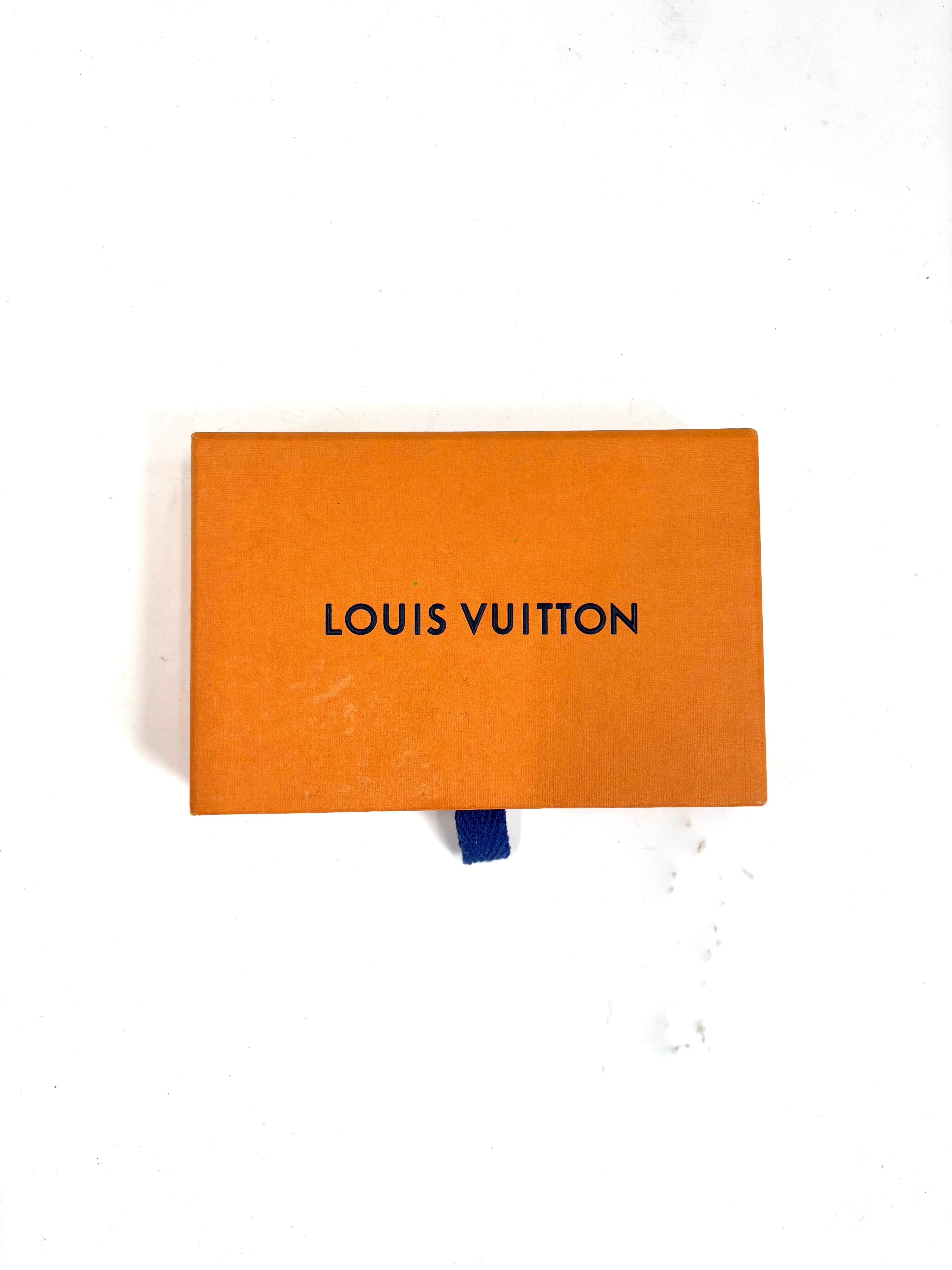 Orange Louis Vuitton box with black lettering and a blue pull tab, placed on a white surface.