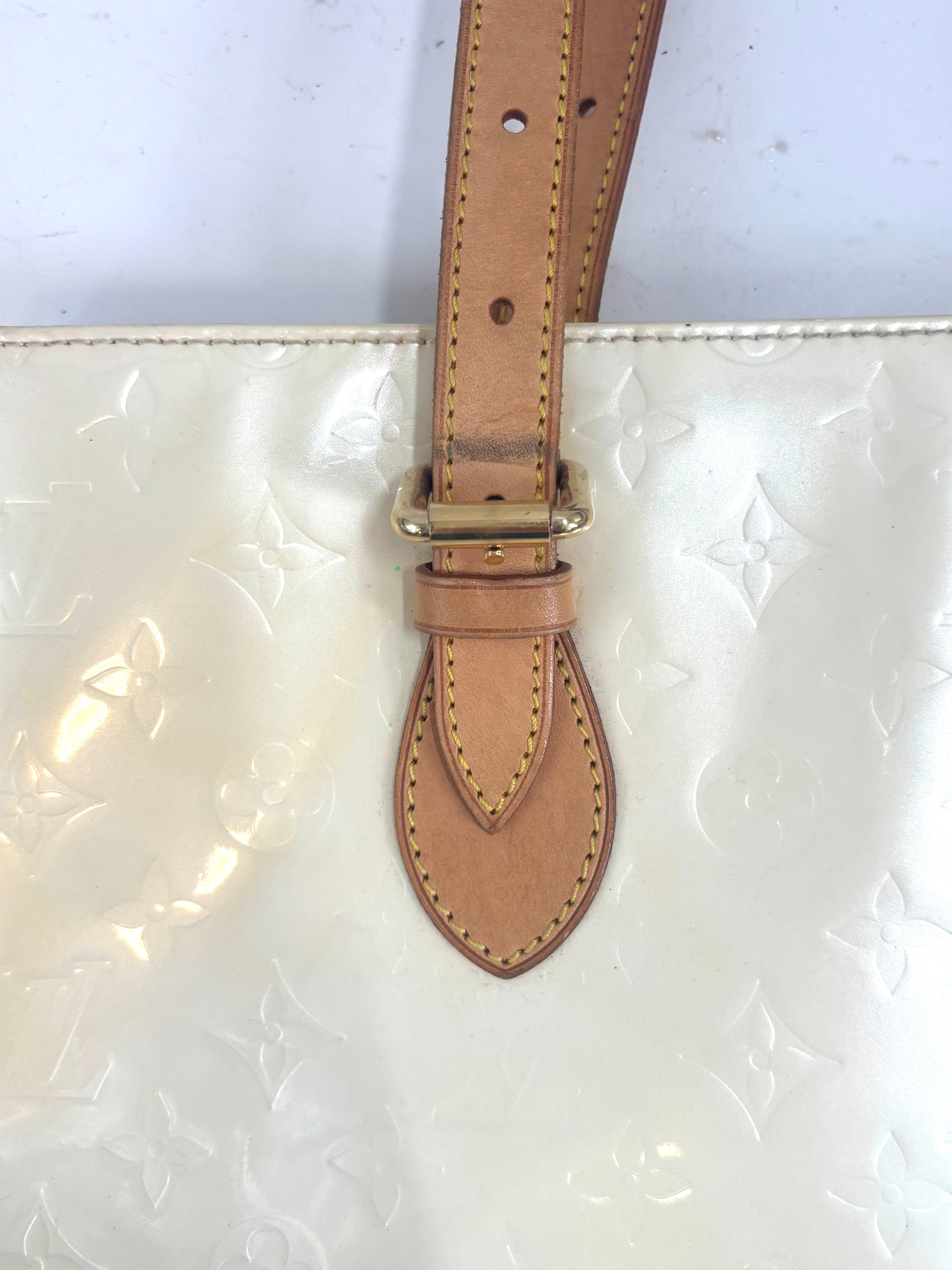 Close-up of a butter yellow Louis Vuitton handbag with shiny leather, embossed floral details, brown strap and gold buckle.