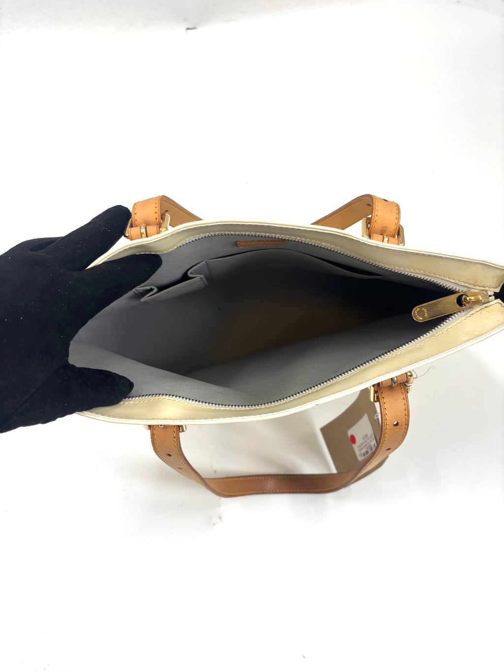 A gloved hand opens a Louis Vuitton yellow handbag, revealing its spacious, empty interior with a side pocket and tan handles.