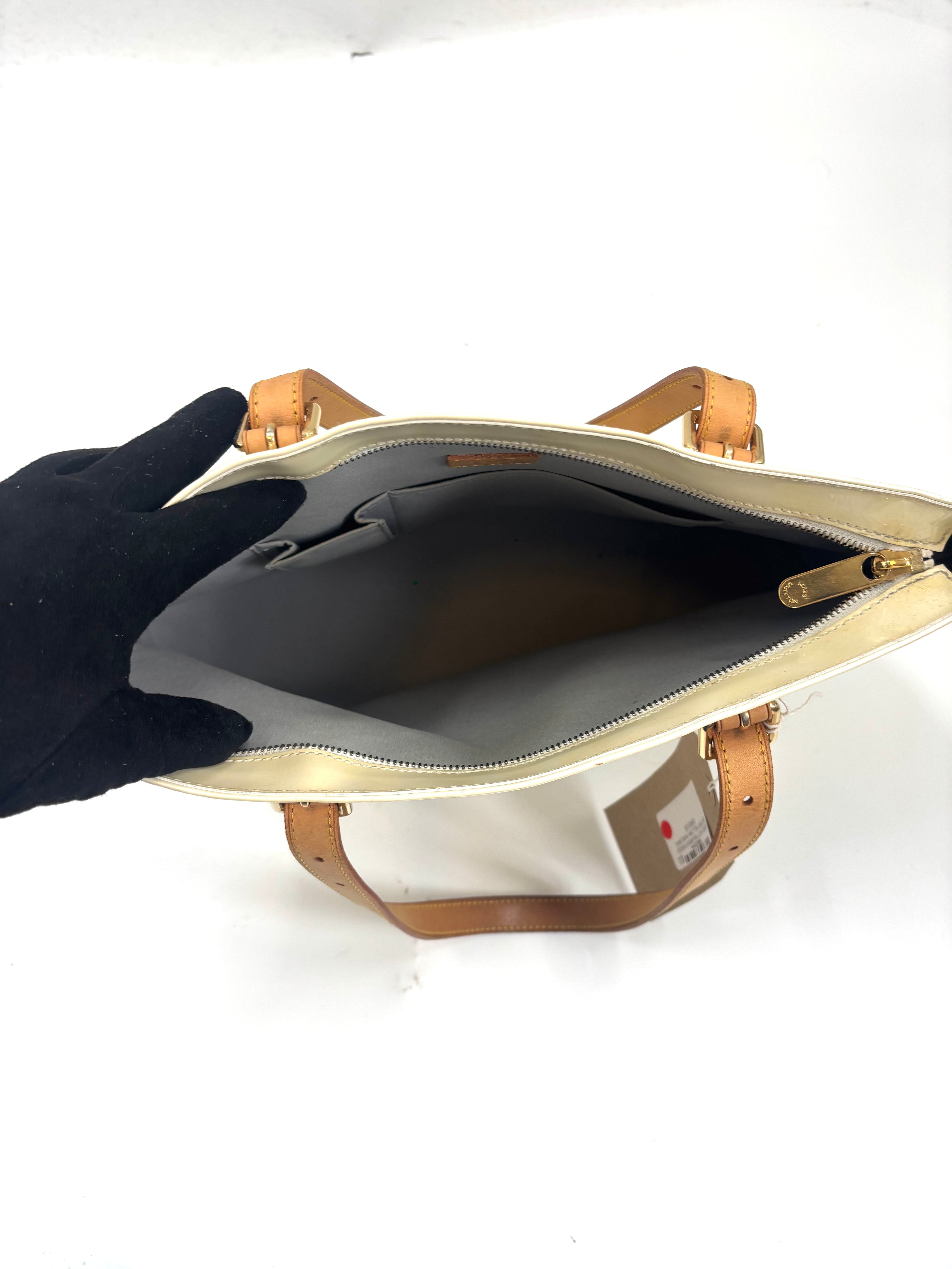 A gloved hand opens a Louis Vuitton yellow handbag, revealing its spacious, empty interior with a side pocket and tan handles.