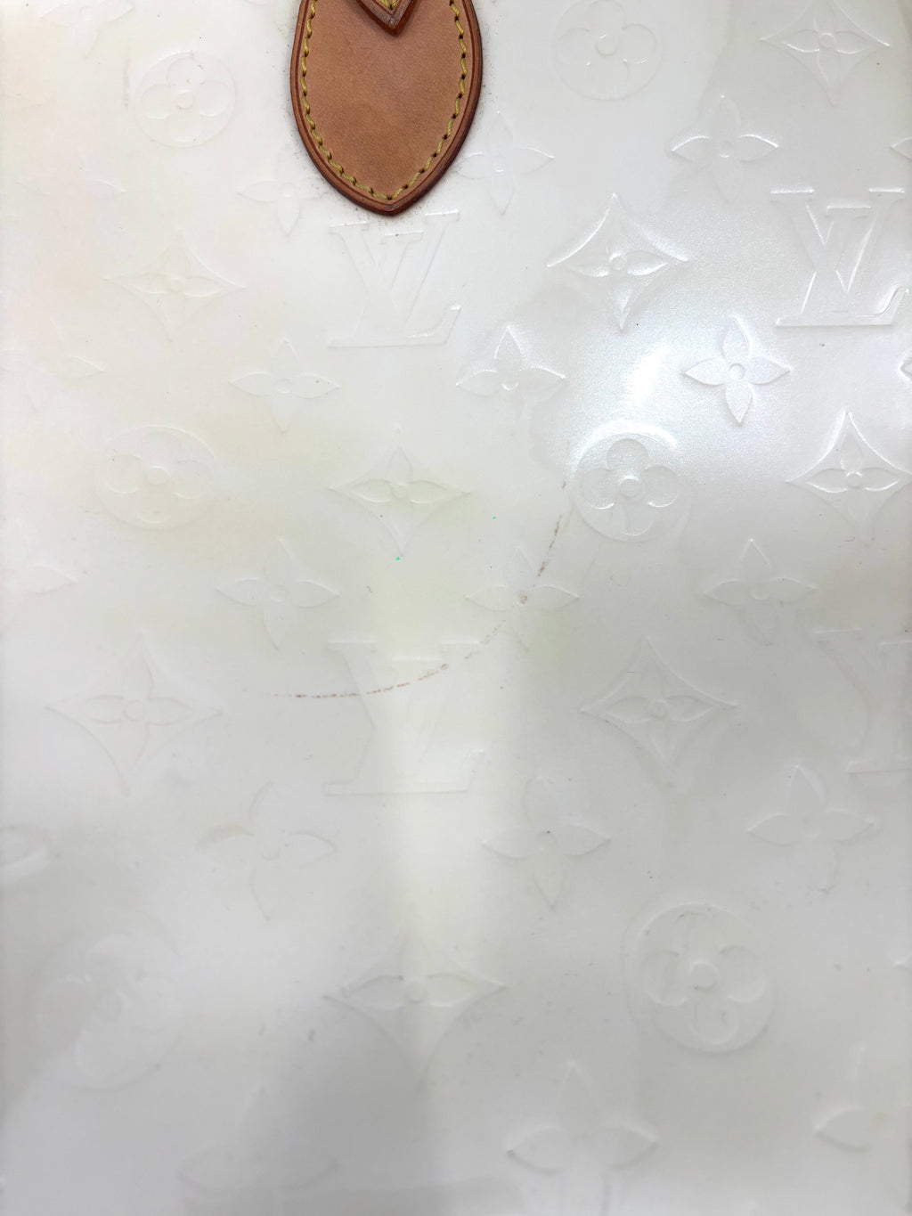 Close-up of a white Louis Vuitton monogrammed surface with a yellow handbag detail at the top and a subtle curved scratch in the centre.