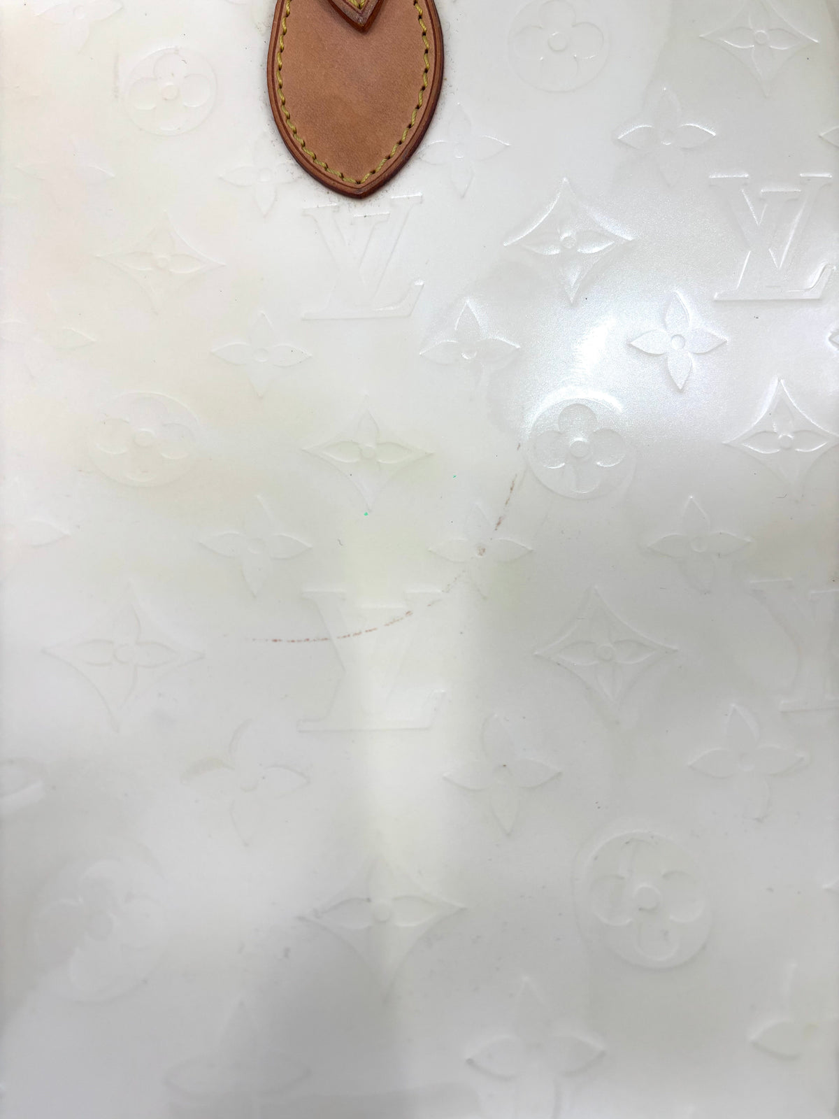 Close-up of a white Louis Vuitton monogrammed surface with a yellow handbag detail at the top and a subtle curved scratch in the centre.