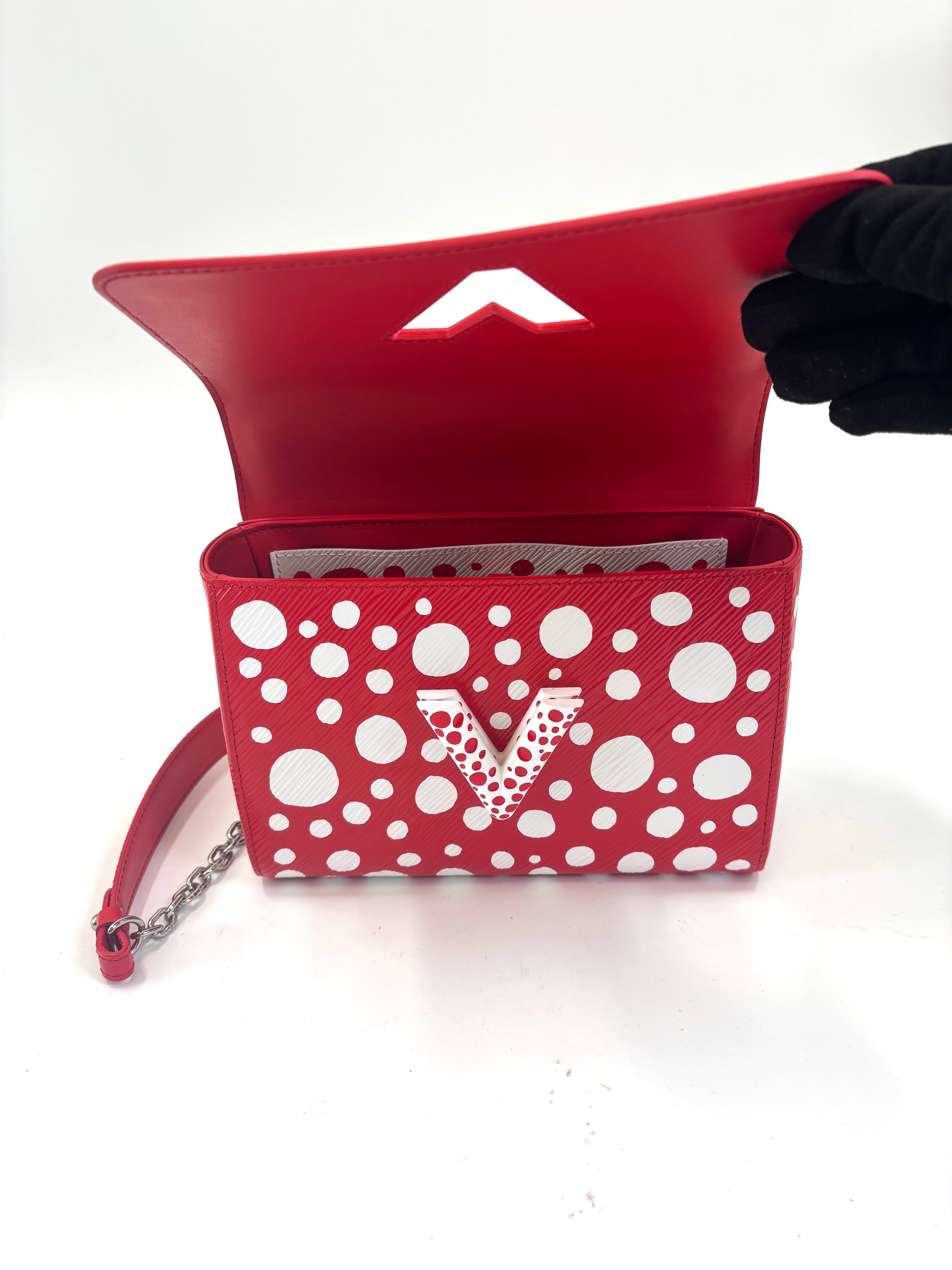 A red Louis Vuitton bag with white polka dots, bold V front, chain strap and geometric white interior, held open by a gloved hand.