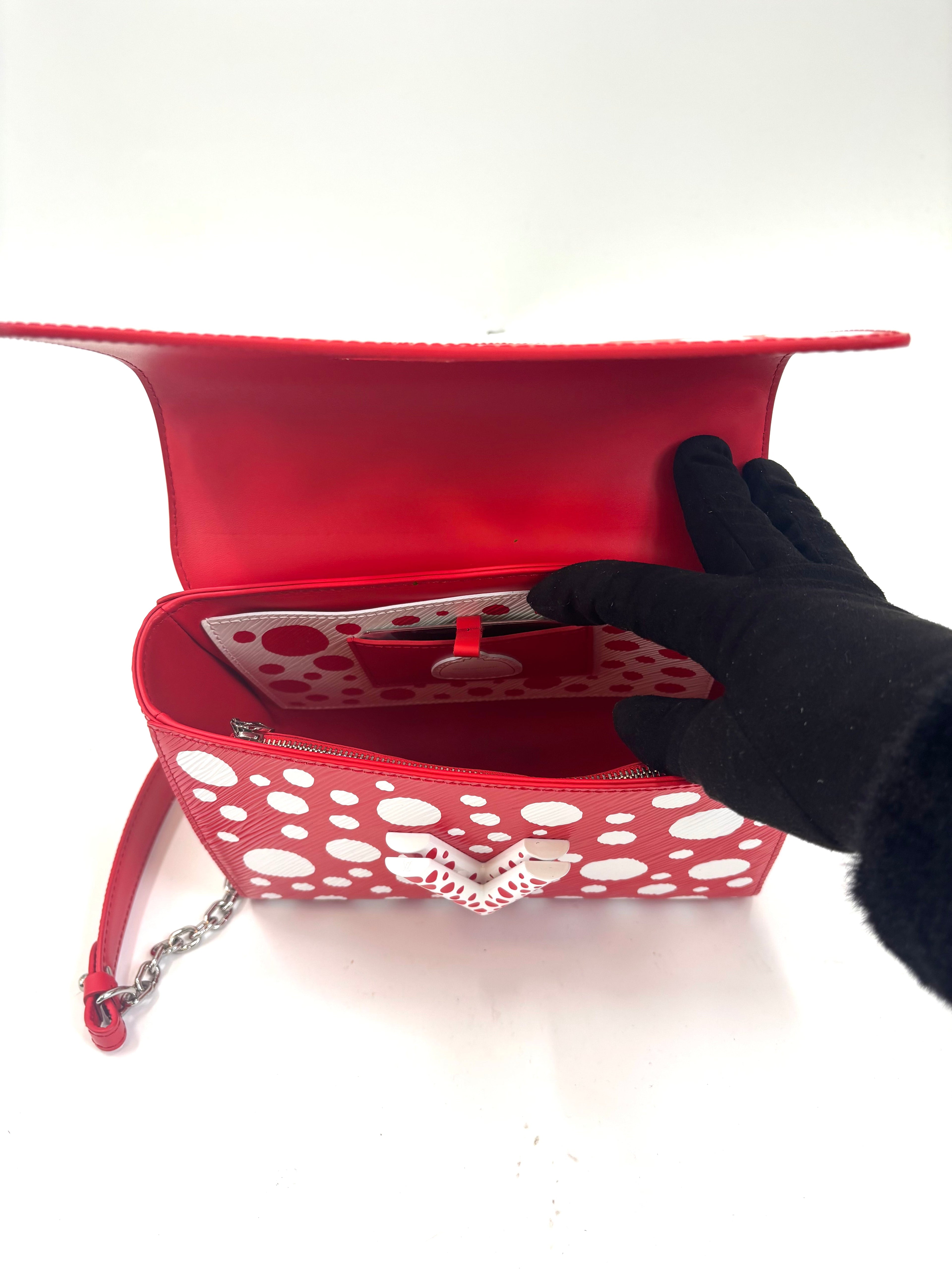 A black-gloved hand opens a Louis Vuitton X Yayoi Kusama bag, showing its red interior with polka dot pocket and silver chain strap.