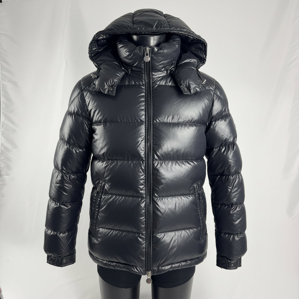 The Moncler Maya jacket is a short, glossy down puffer known for its boxy fit, strong insulation, detachable hood, and