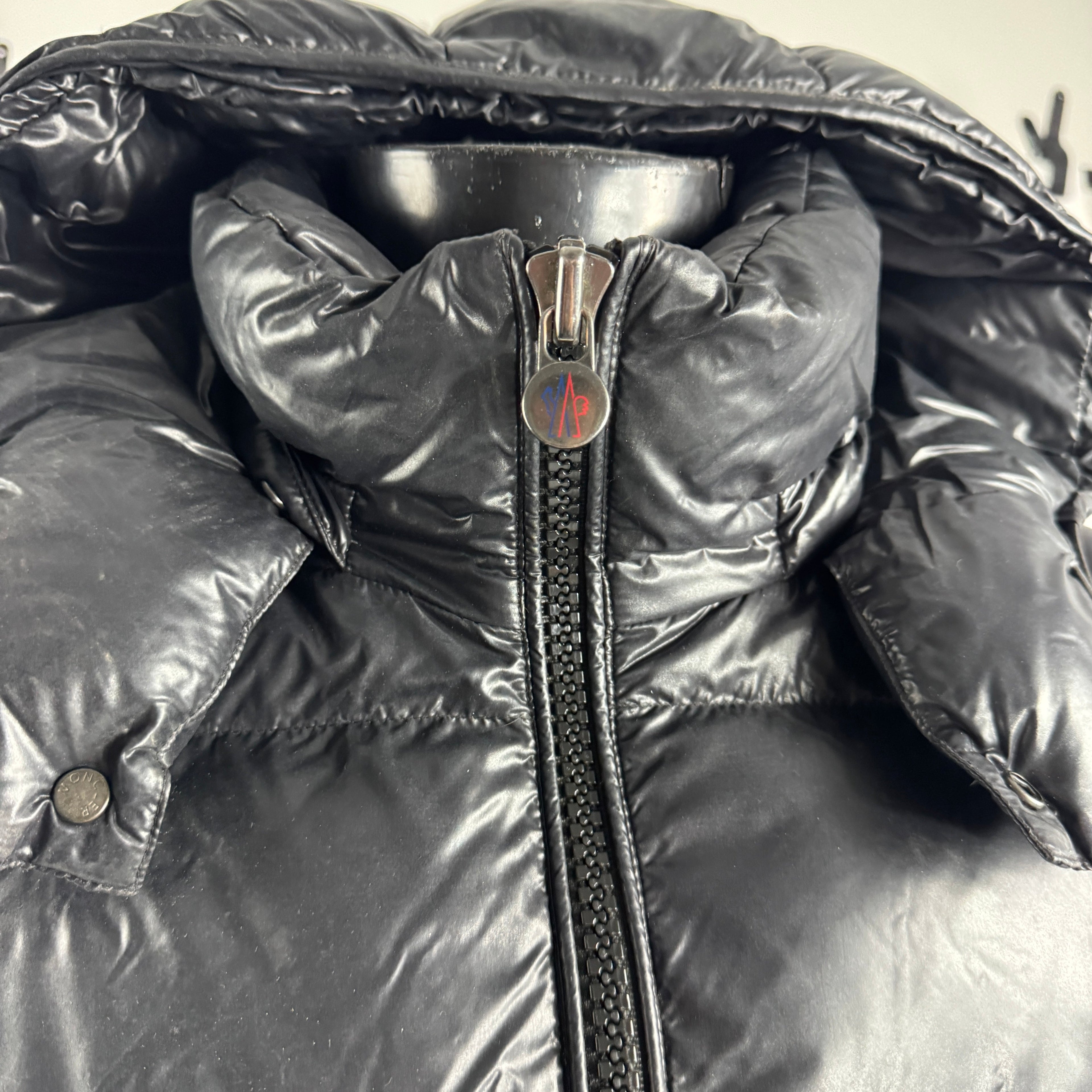 The Moncler Maya jacket is a short, glossy down puffer known for its boxy fit, strong insulation, detachable hood, and