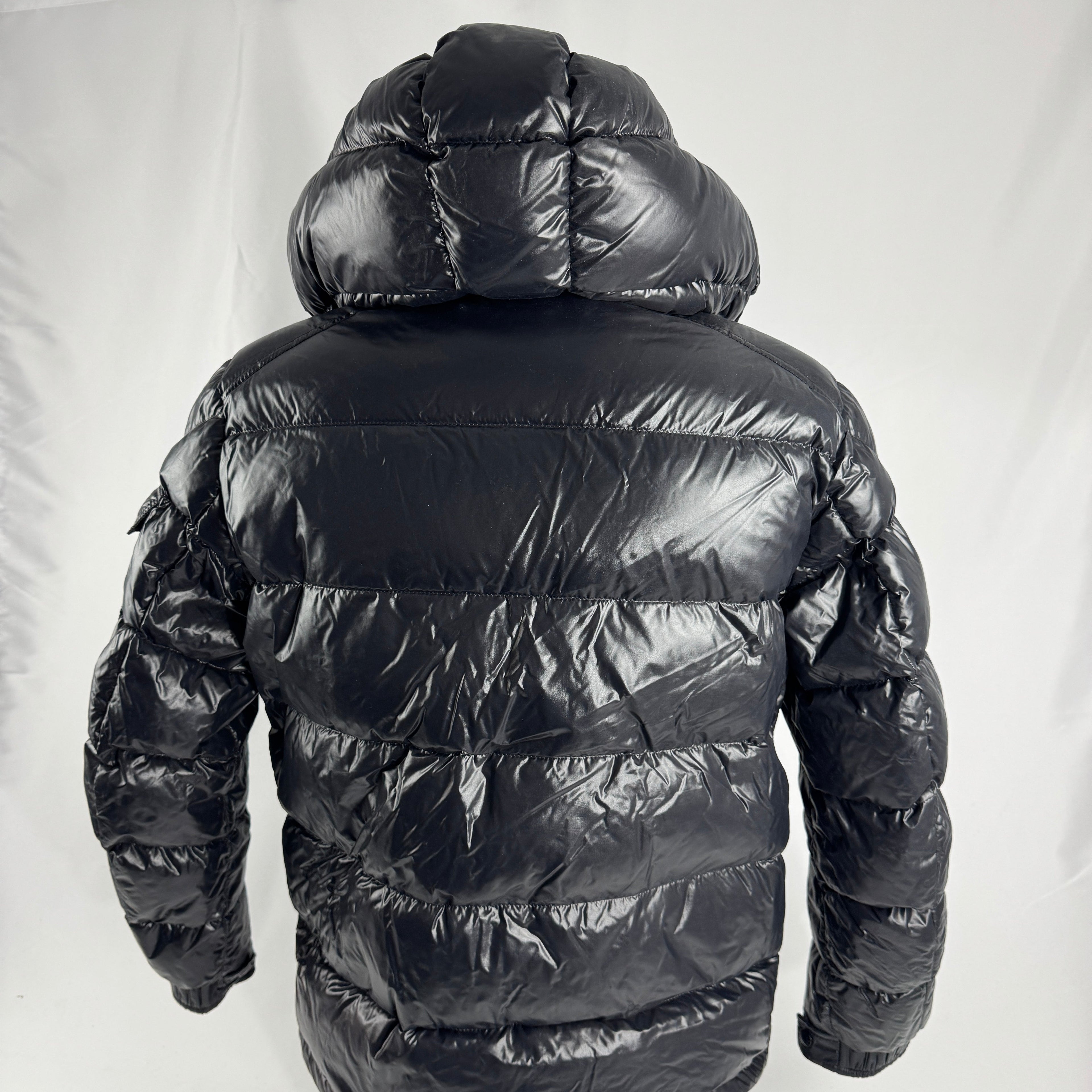 The Moncler Maya jacket is a short, glossy down puffer known for its boxy fit, strong insulation, detachable hood, and