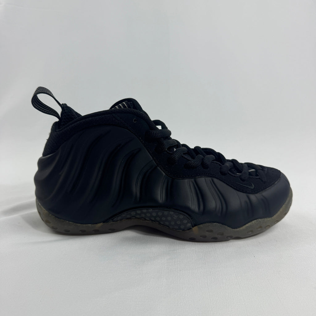 A black Nike trainer with wavy textured sides, black laces, heel pull tab and a translucent sole on a plain white background.