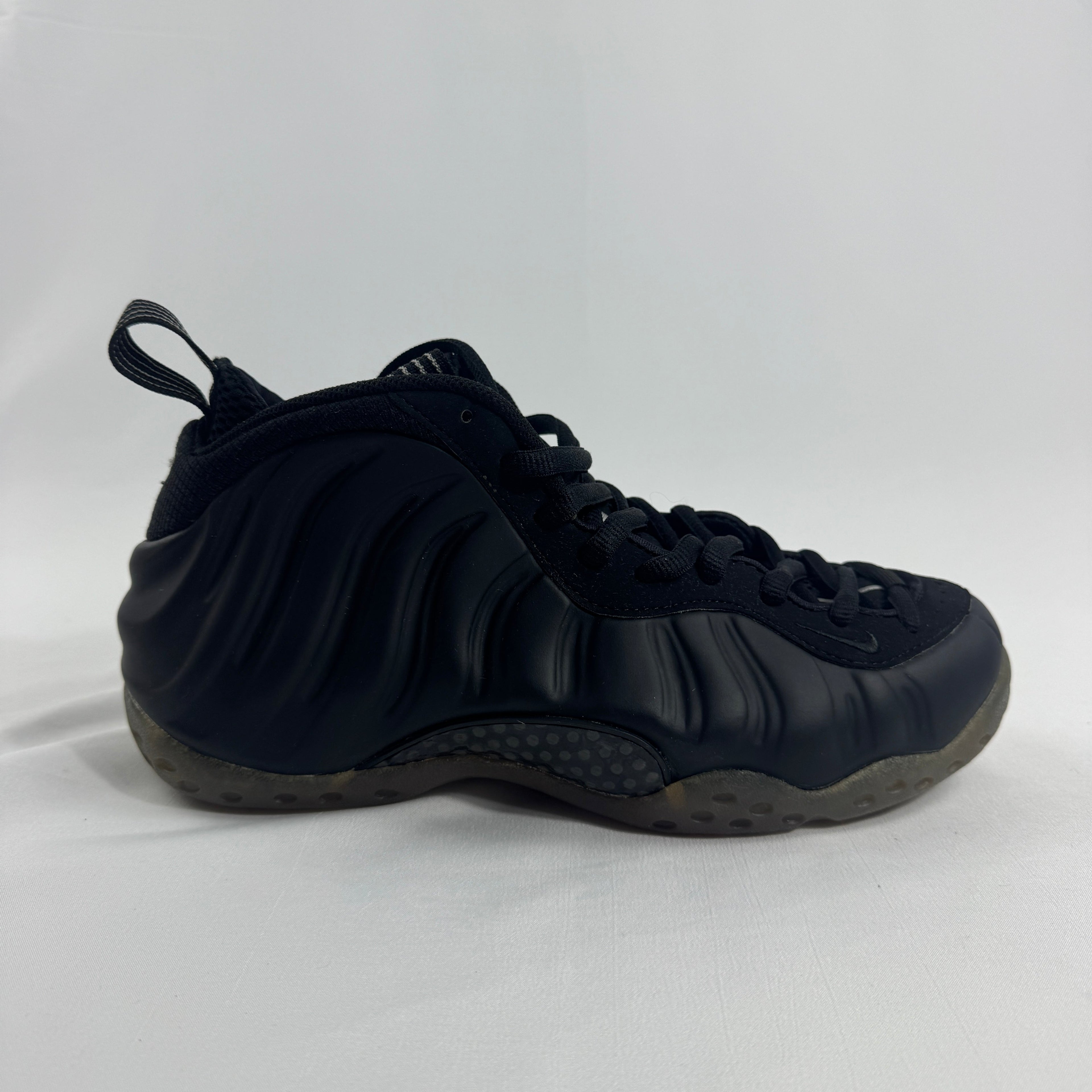 A black Nike trainer with wavy textured sides, black laces, heel pull tab and a translucent sole on a plain white background.